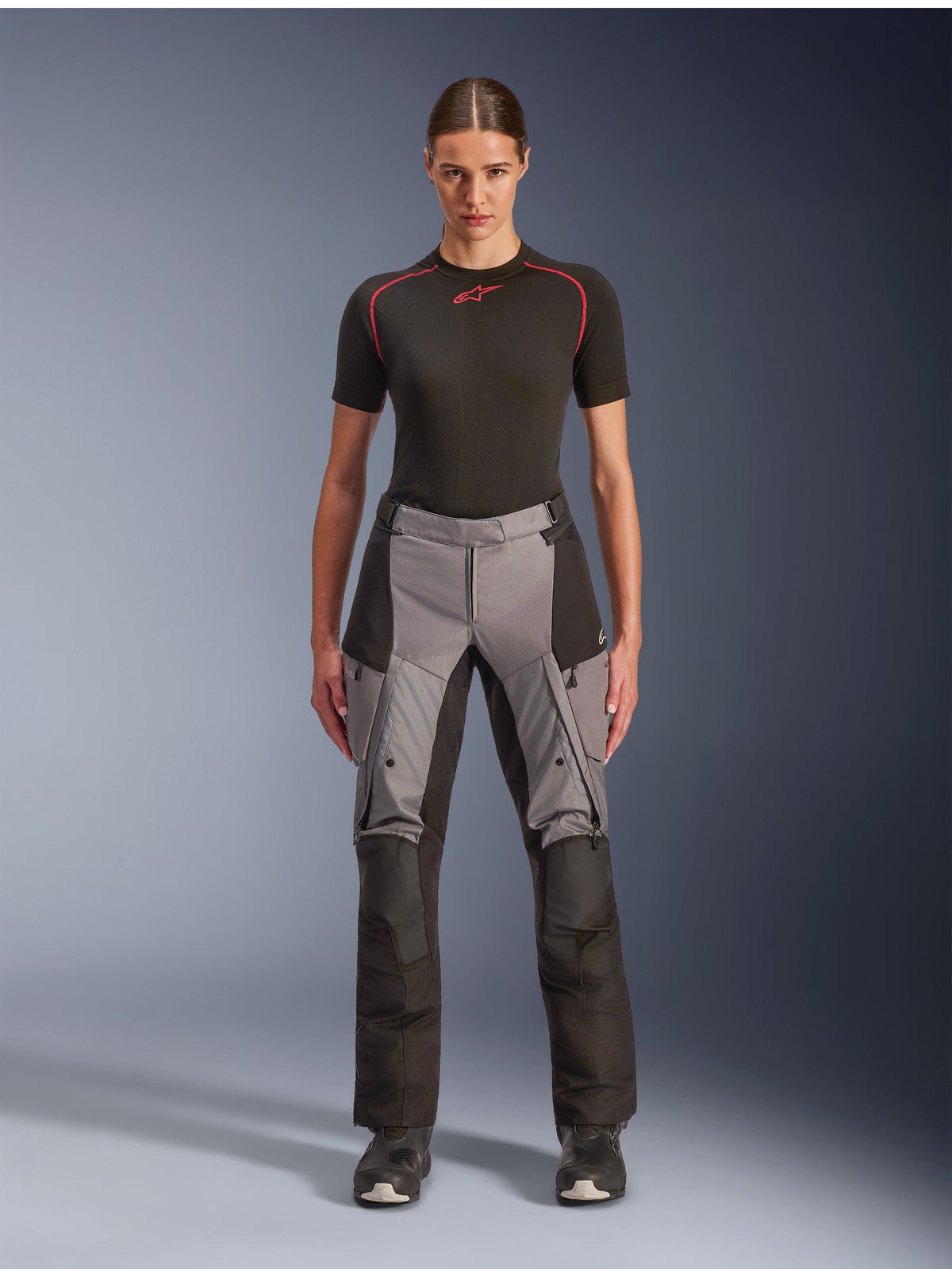 Calças Alpinestars Stella Andes V4 Drystar, calças de motociclismo touring de aventura para mulher, pretas e cinzento escuro, vestidas por uma modelo com uma camada base preta e botas de motociclista, apresentando painéis têxteis reforçados e bolsos cargo para condução de aventura