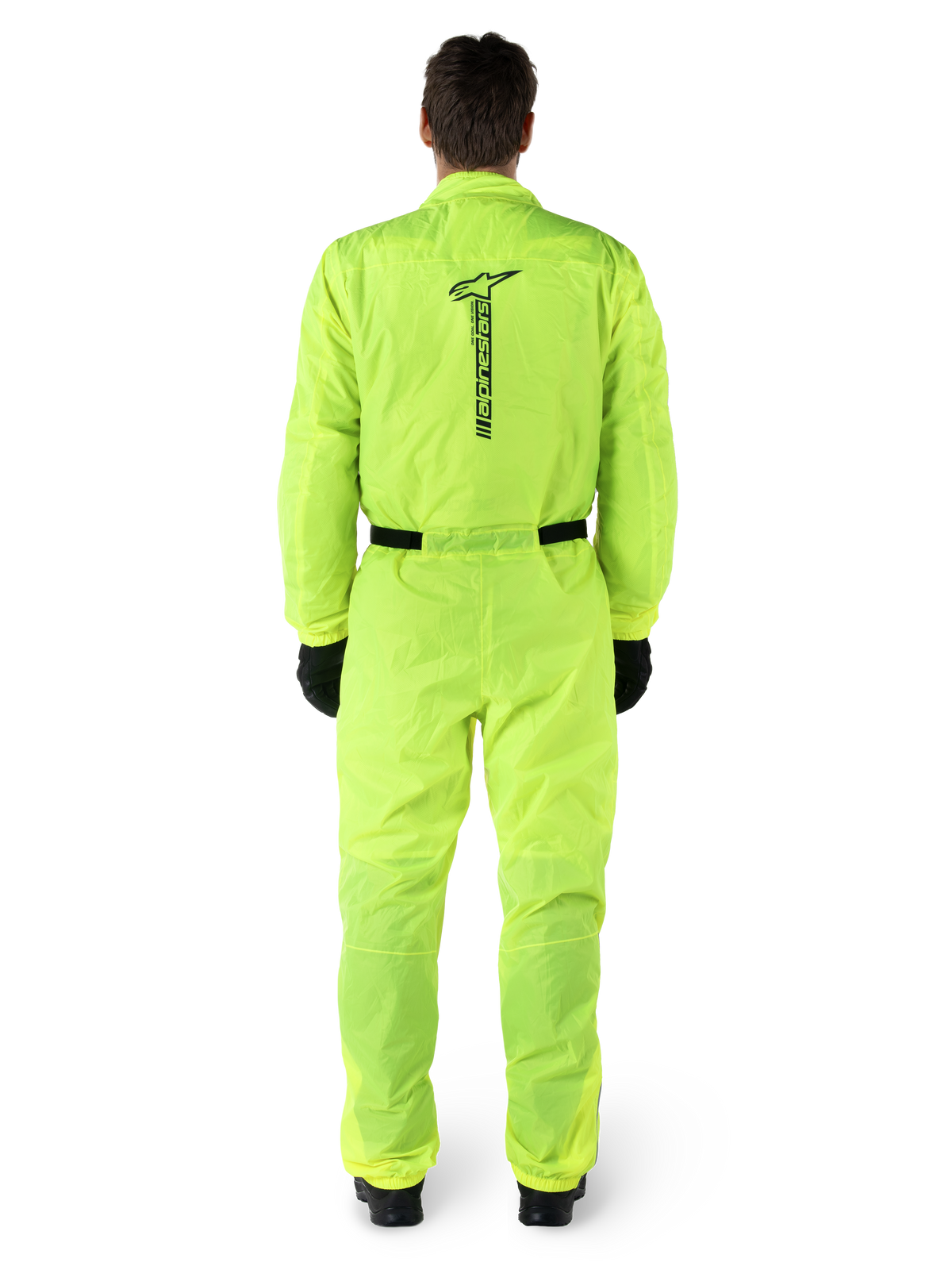 Fato Alpinestars Hurricane Rain V2, fato impermeável de motociclismo de uma peça, Amarelo Fluo, vista traseira com marca Alpinestars vertical a preto, cintura e punhos elásticos, usado com luvas e botas pretas, equipamento de condução impermeável e resistente ao vento