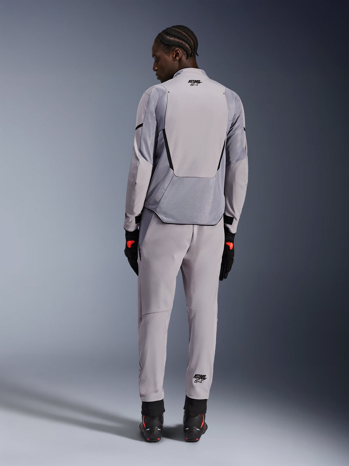 Casaco Alpinestars Aeroshell Airflow, Cinzento Médio Antracite, vista traseira num modelo, com painéis de malha técnica e zonas de ventilação perfuradas a laser, usado com calças cinzentas a condizer e equipamento de motociclismo preto, design de corte desportivo para alto desempenho.