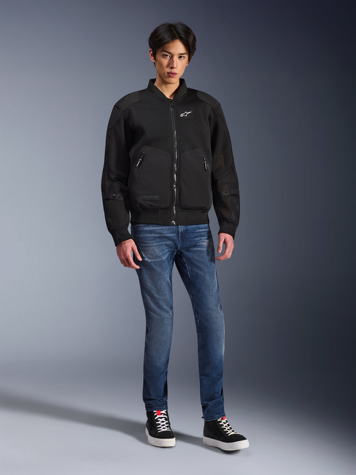 Casaco Alpinestars Flight Air, Preto, casaco de motociclista estilo bomber de inspiração urbana com painéis de malha 3D e logótipo branco no peito, usado por um modelo com calças de ganga azuis e sapatilhas pretas, vestuário de condução contemporâneo