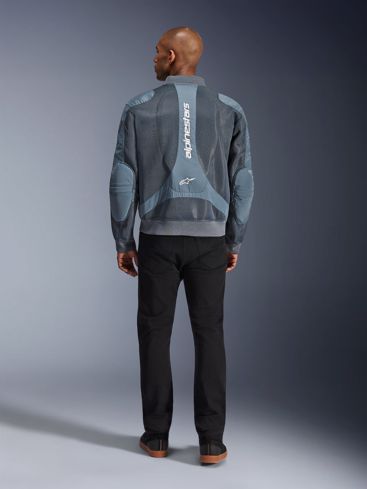 Alpinestars Flight Air Jacket em Storm Gray, vista traseira de modelo masculino a usar casaco de motociclismo de estilo urbano com painéis de malha 3D e logótipo Alpinestars vertical, combinado com calças pretas para um visual urbano moderno