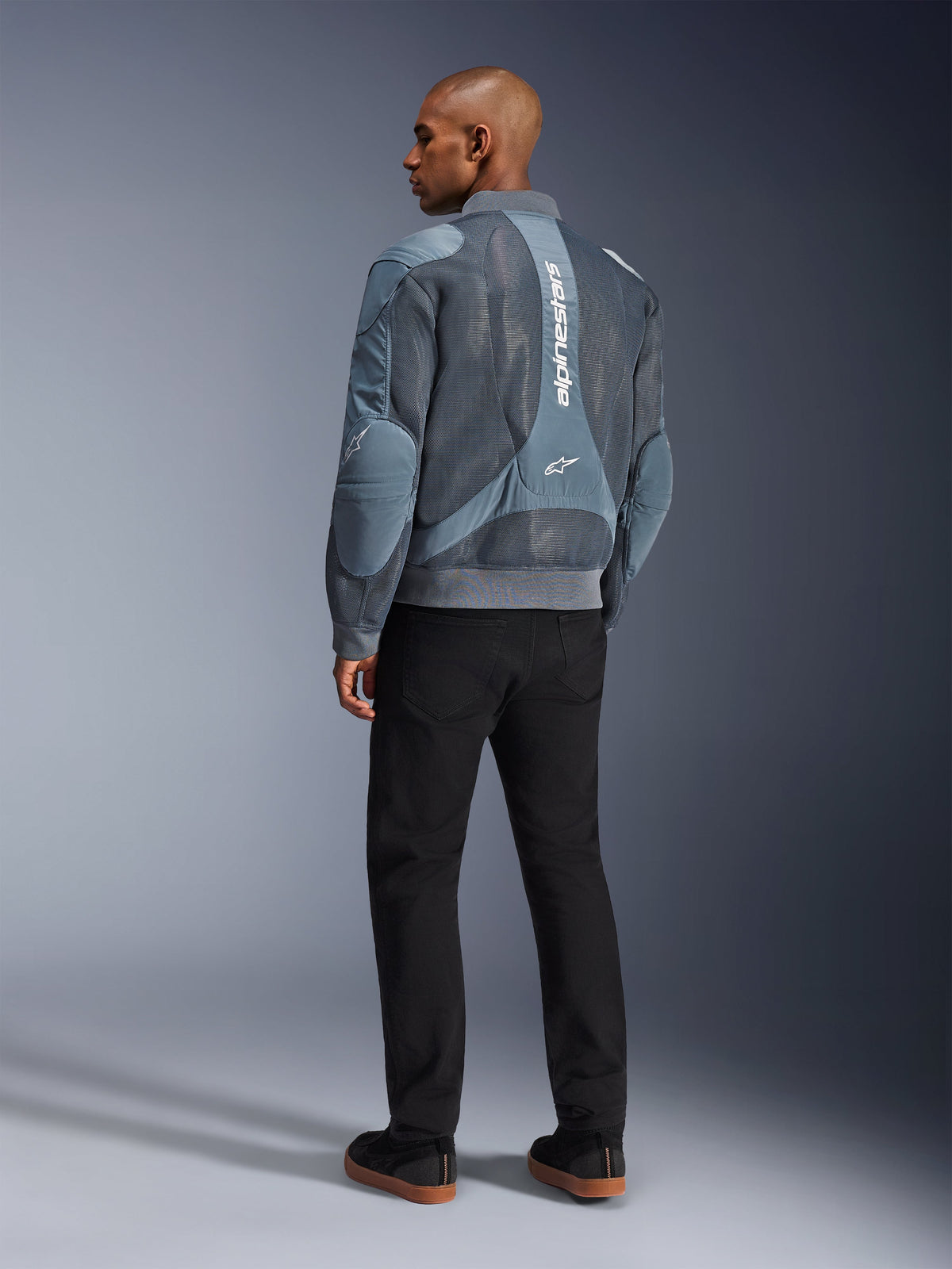 Casaco Alpinestars Flight Air, casaco de motociclismo Storm Gray, vista traseira, com painéis de ventilação em malha 3D e marca Alpinestars branca vertical, usado com calças pretas e ténis pretos, estilo urban commuter