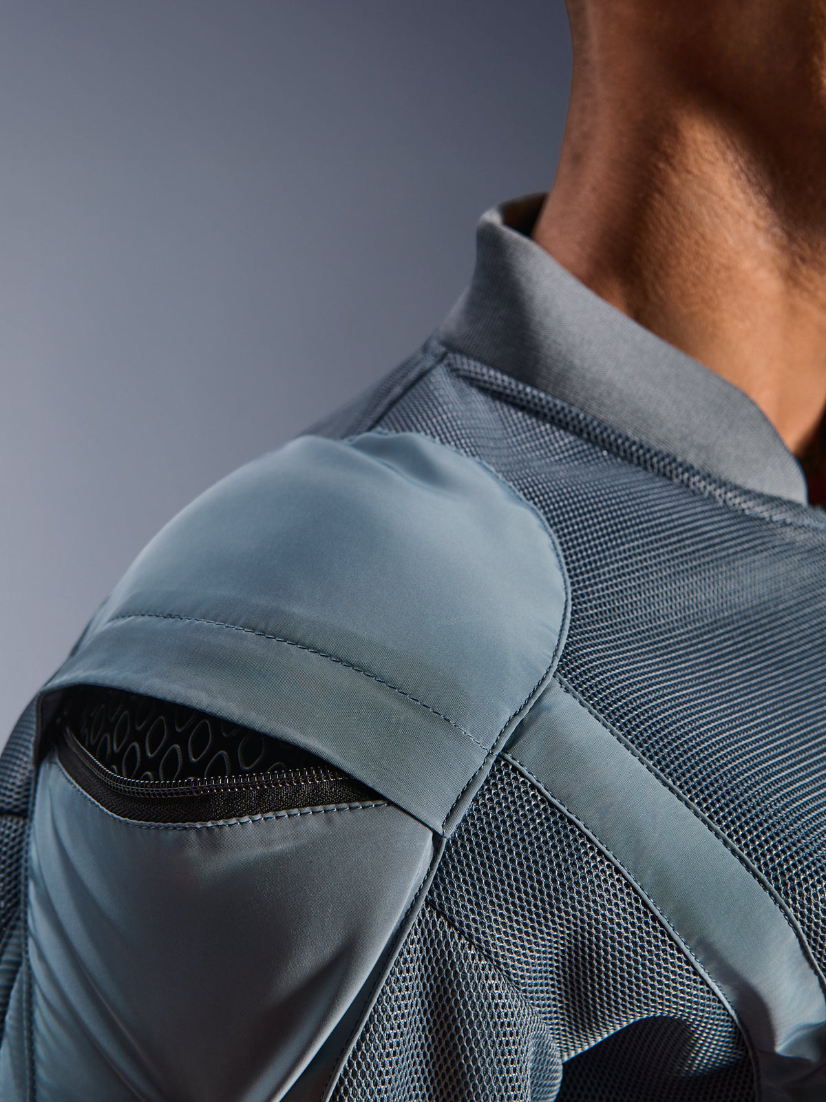 Pormenor do casaco Alpinestars Flight Air Jacket em Storm Gray, realçando o bolso externo para o protetor de ombro com armadura em favo de mel visível, painéis de ventilação em malha 3D e gola canelada para condução urbana técnica de motociclo