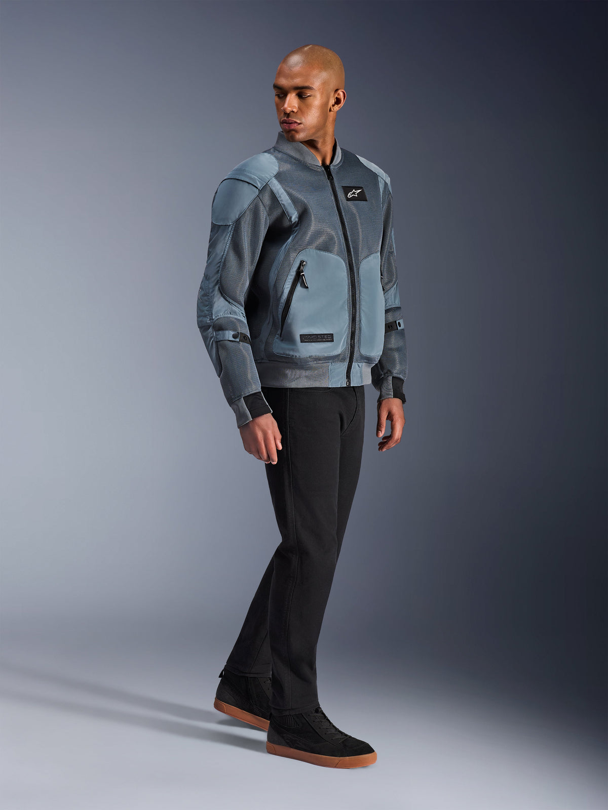Alpinestars Flight Air Jacket, Storm Gray, casaco de motociclismo de inspiração bomber urbana, usado por um modelo masculino com calças pretas e sapatilhas, com painéis de ventilação em malha 3D alargados e bolsos externos para proteções, equipamento de proteção streetwear moderno para condução em tempo quente