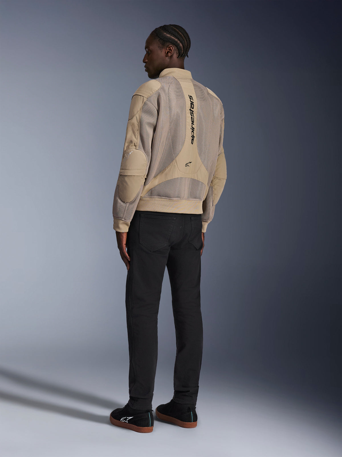 Alpinestars Flight Air Jacket, urban textile motorcycle jacket, Brown, back view showing large 3D mesh panels and vertical logo, bomber-style silhouette with ribbed collar and hem, paired with black pants and black shoes for street-inspired riding style.