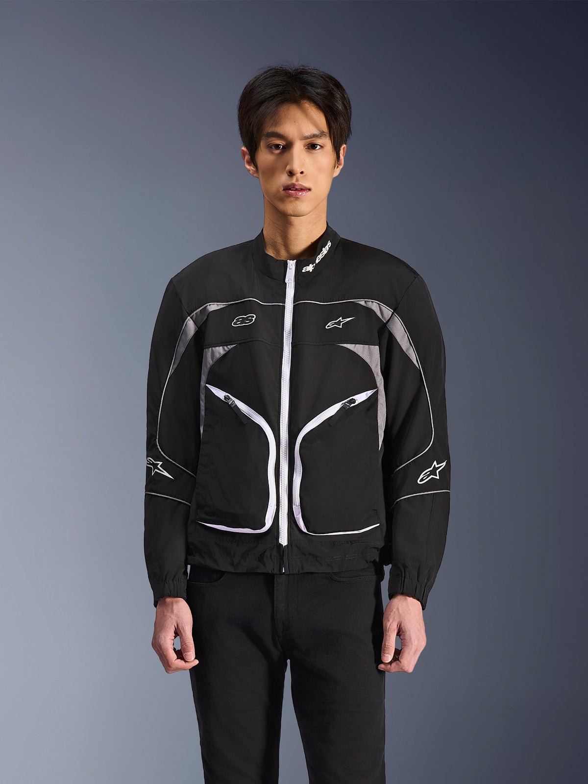 Casaco Alpinestars Unite, casaco de motociclismo urbano minimalista, preto e cinzento escuro com detalhes brancos, apresenta fecho de correr frontal branco, frisos refletores e logótipos Alpinestars no peito e nas mangas, estilo streetwear contemporâneo para motociclistas