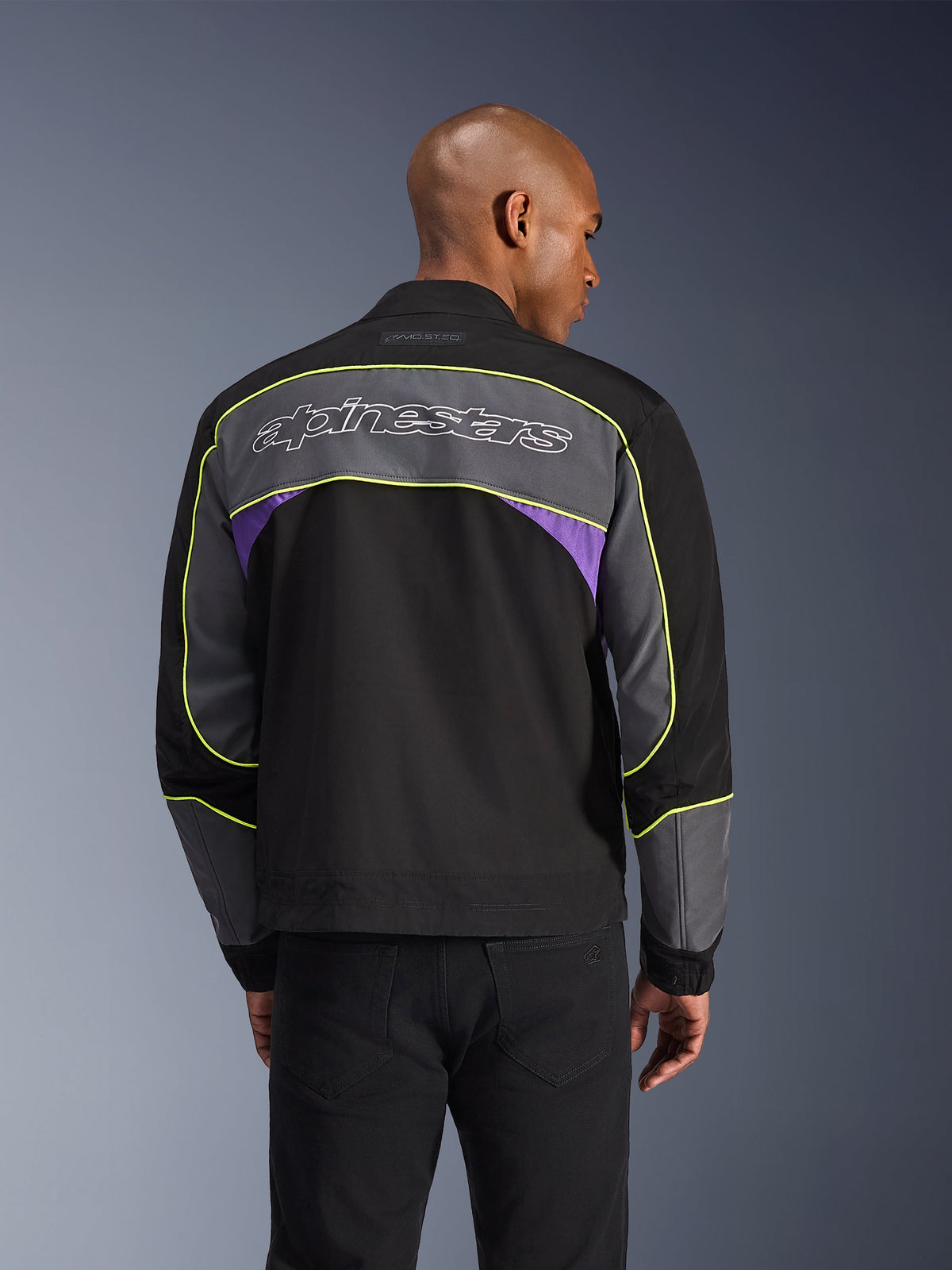 Casaco Alpinestars Unite, casaco de motociclismo urbano, Black Asphalt Violet, vista traseira com painéis cinzentos e detalhes violeta, vivo amarelo lima, logótipo Alpinestars de grandes dimensões na parte superior das costas, design streetwear minimalista