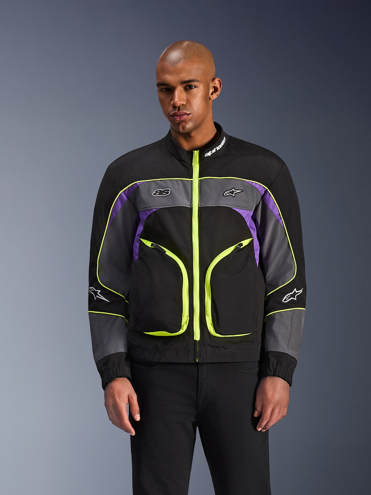 Alpinestars Unite Jacket, casaco de motociclismo urbano, preto Asphalt e violeta com detalhes em amarelo néon, com grandes bolsos frontais e fechos néon, gola alta com logótipo branco, vestido por modelo, equipamento de proteção contemporâneo inspirado em streetwear