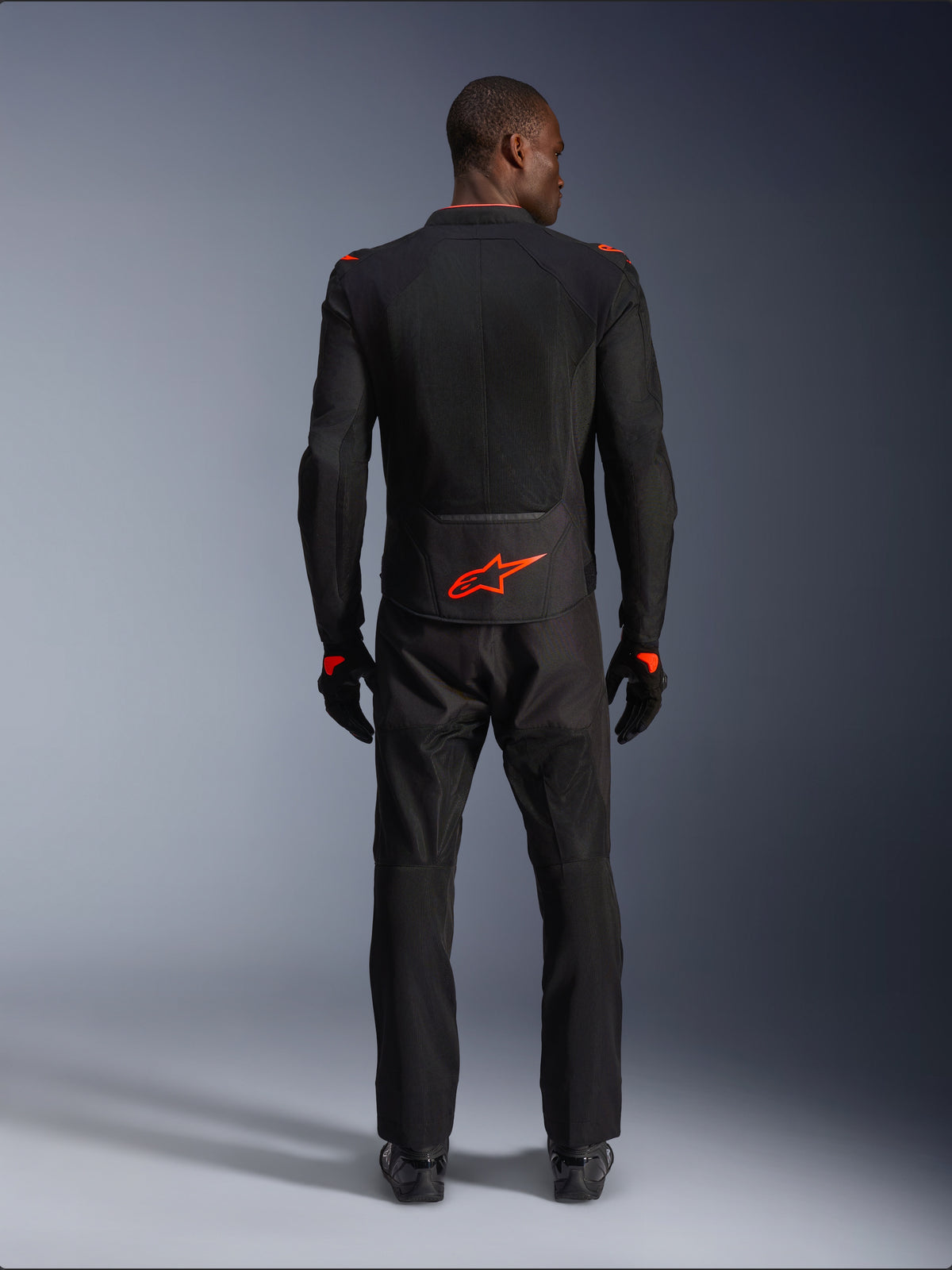 Casaco Alpinestars Viper Air V4, Preto e Vermelho Fluo, vista traseira no modelo, usado com calças de condução e luvas pretas a condizer, com logótipo vermelho fluorescente na zona lombar, construção em malha para fluxo de ar, ajuste atlético para condução de estrada