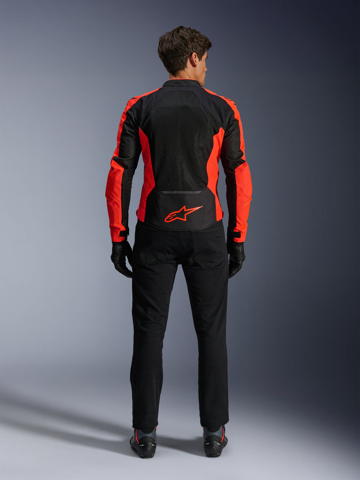 Casaco Alpinestars Viper Air V4, Vermelho Fluo e Preto, vista traseira realçando grandes painéis de malha técnica e pormenores laterais em vermelho fluorescente, logótipo Alpinestars vermelho na zona lombar, usado com calças e luvas de condução pretas