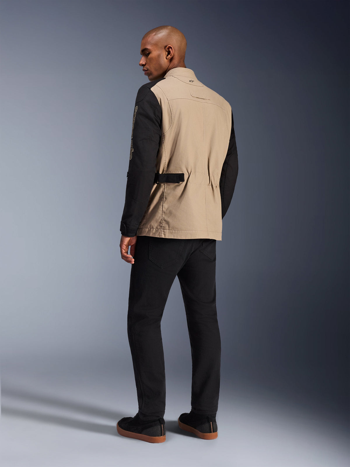 Alpinestars Dice Jacket, Urban Motorcycle Jacket, Aluminum Black with tan torso and black sleeves, back view on model, rugged workwear-inspired design featuring waist adjusters, paired with black riding pants.