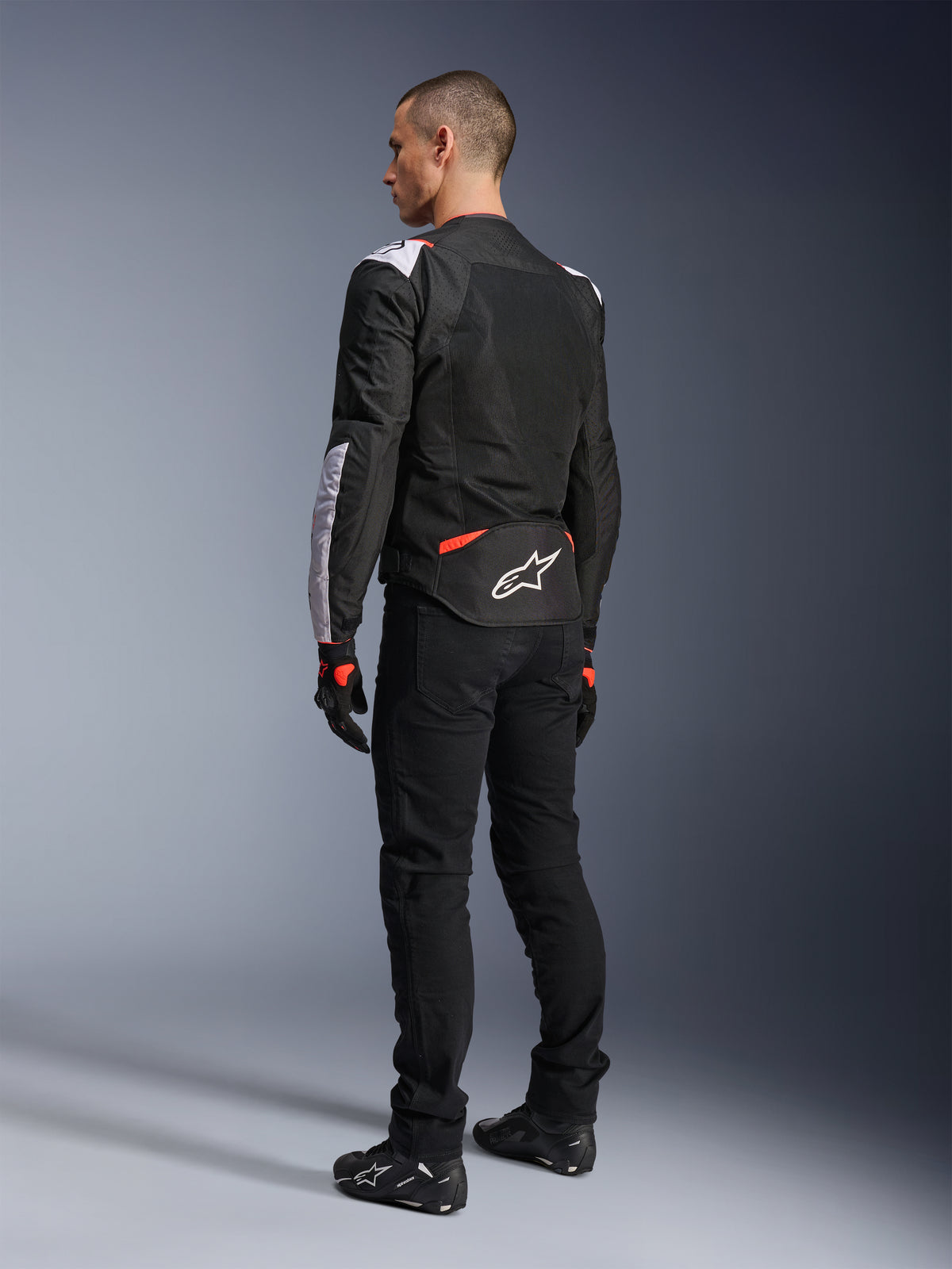 Casaco Alpinestars T-Sps Air V2, casaco de motociclismo têxtil, preto, branco e vermelho fluorescente, vista traseira no modelo, painéis em malha para ventilação, logótipo Astars branco na parte inferior das costas, combinado com calças de condução e luvas pretas