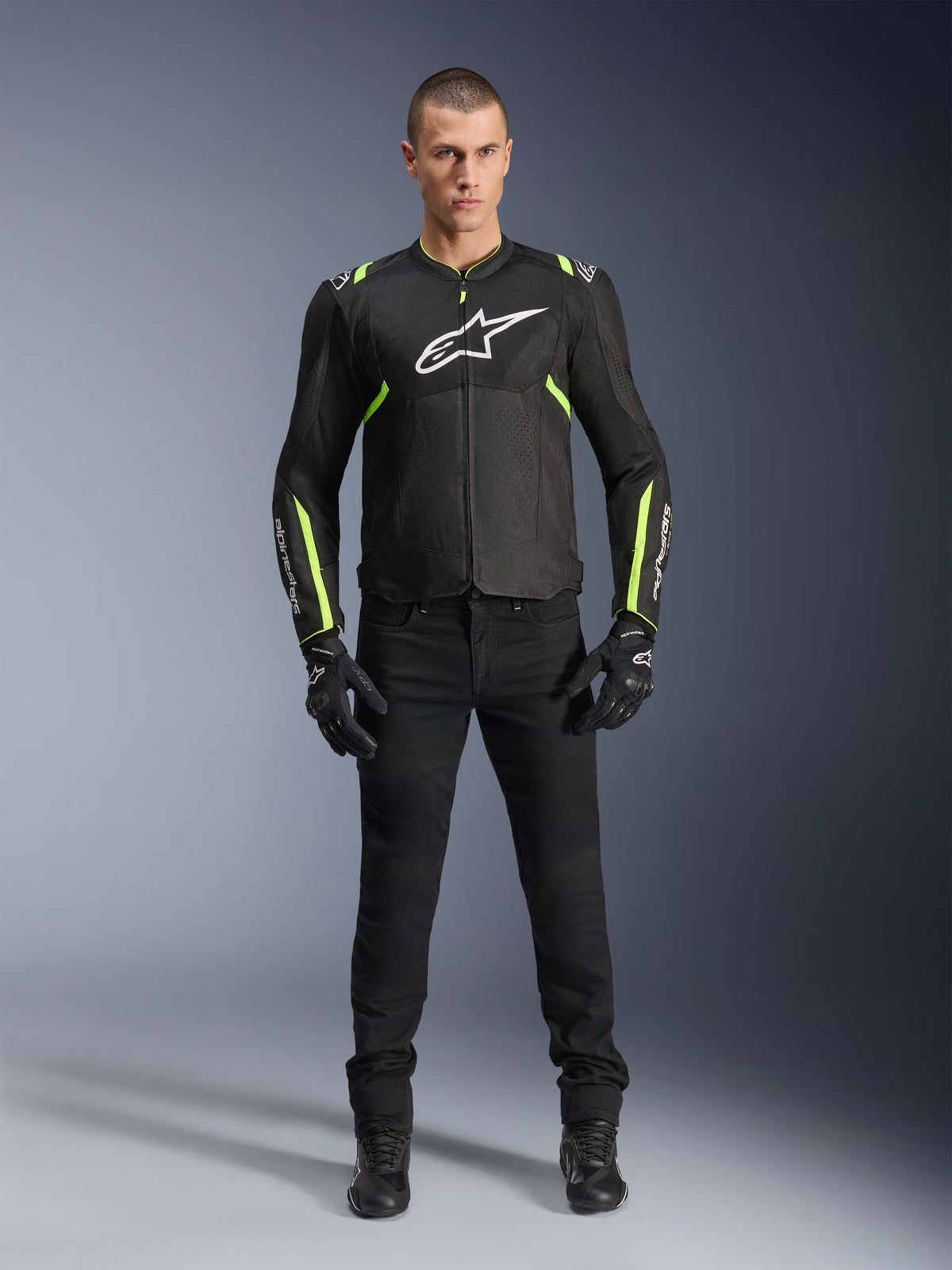 Casaco Alpinestars T-Sps Air V2, preto e amarelo fluorescente, casaco de motociclismo têxtil com painéis de malha, usado por modelo masculino com calças e luvas pretas, com logótipo branco da Alpinestars no peito, equipamento de condução desportiva urbana