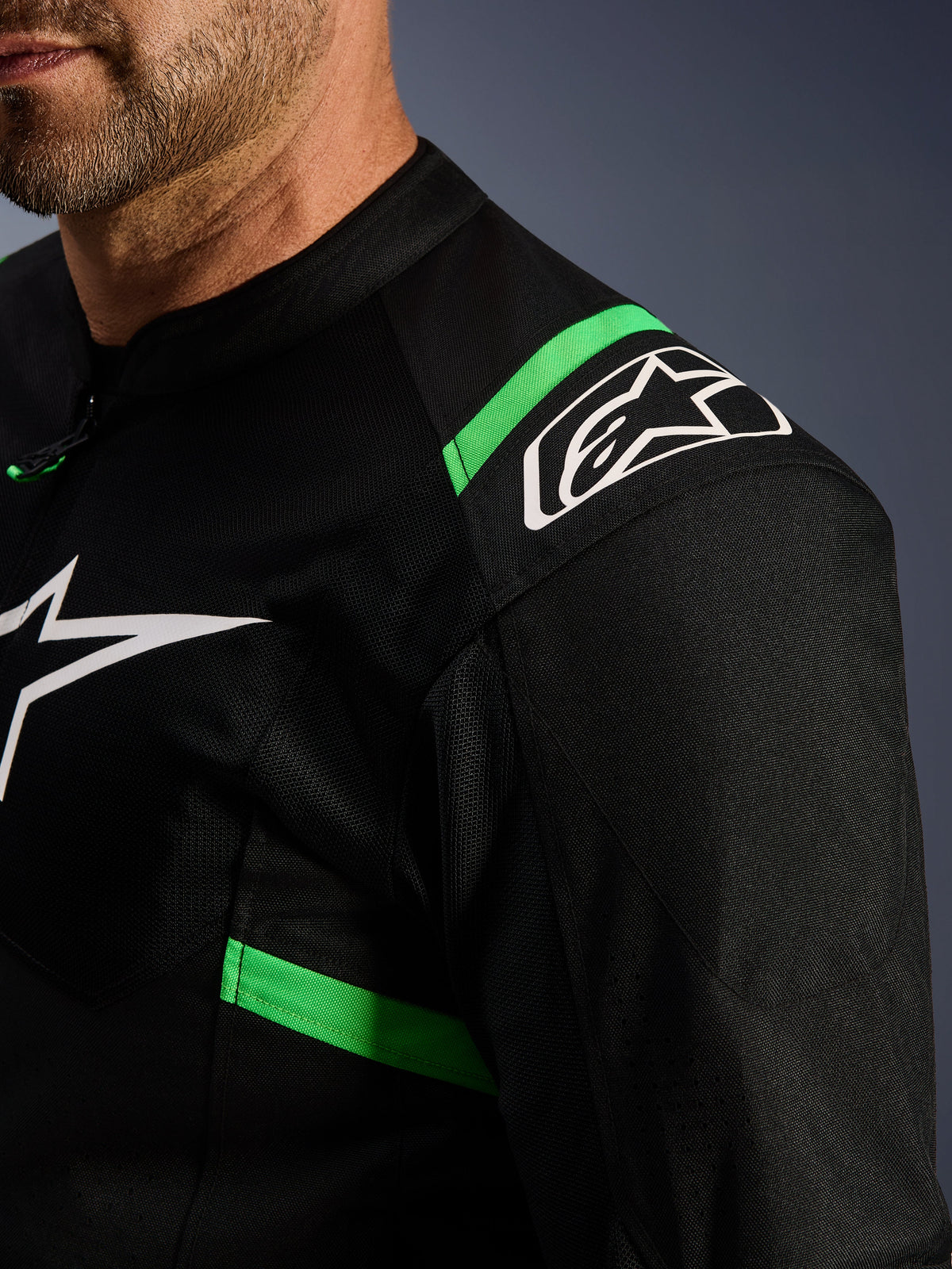 Casaco Alpinestars T-SPS Air V2, preto e verde fluorescente, pormenor da zona do ombro e do peito, logótipo da estrela Alpinestars a branco, tecido de malha técnica para circulação de ar, casaco de motociclismo desportivo