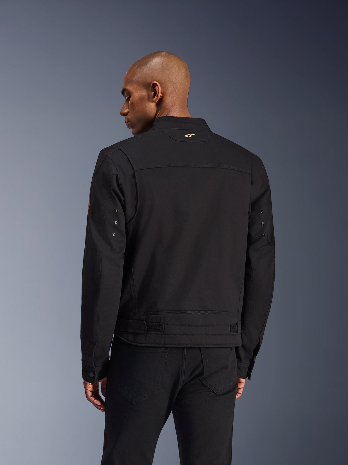 Alpinestars Bruiser Jacket, Black Urban Motorcycle Jacket, back view, featuring a workwear-inspired design with a small gold logo on the collar and adjustable waist straps, durable textile construction for urban riding