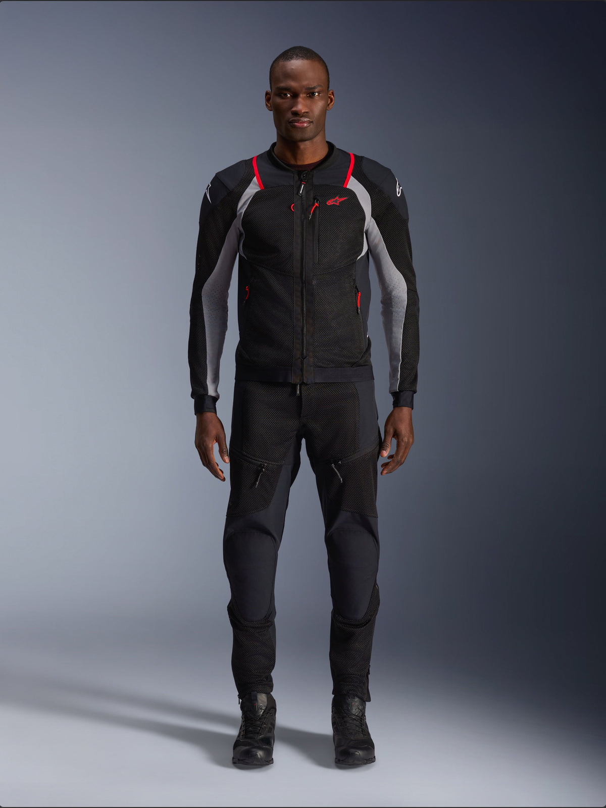 Alpinestars Troop-Air Pro Jacket, casaco técnico de motociclismo, preto, cinzento ash e vermelho vivo, com painéis de malha e pormenores em vermelho, vestido por modelo masculino com calças e botas de motociclismo pretas, design urbano elegante com ventilação técnica.