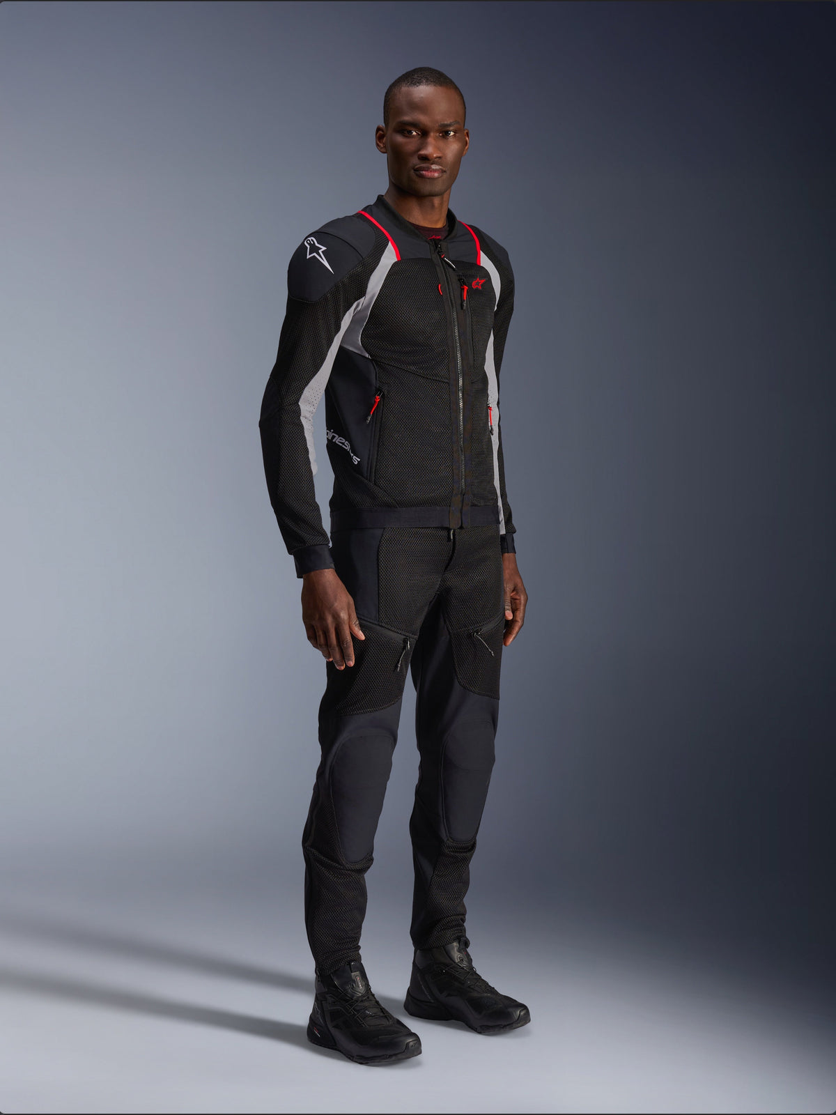 Casaco Alpinestars Troop-Air Pro, Preto, Cinzento Ash e Vermelho Vivo, casaco técnico de malha com proteção, com detalhes vermelhos e logótipo branco no ombro, usado com calças e botas pretas a condizer, vestuário de motociclismo urbano moderno