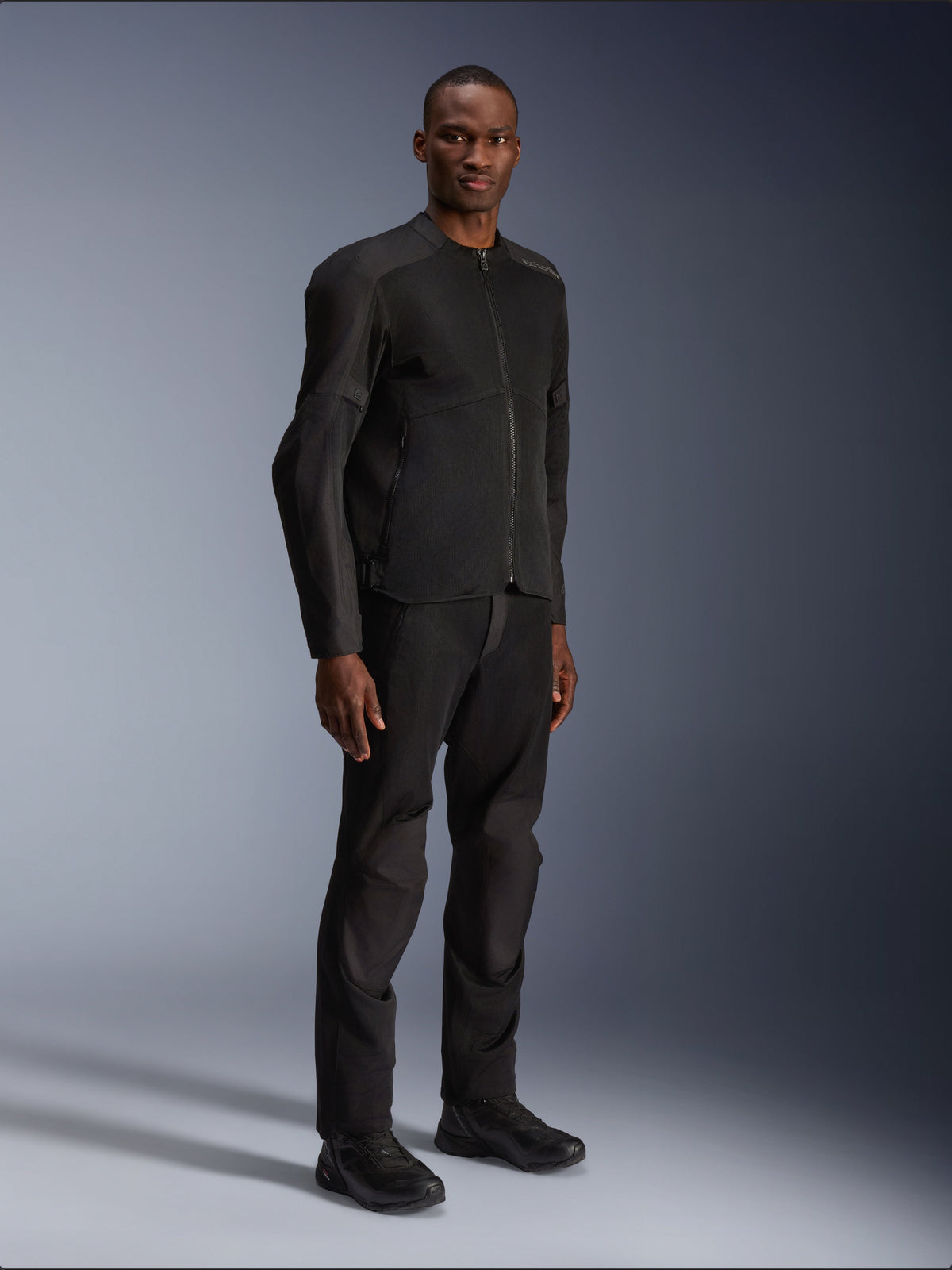 Casaco Alpinestars C-1 Air, preto, vestido por um modelo com calças e sapatos de motociclismo pretos a condizer, com amplos painéis de malha técnica para circulação de ar, estética urbana limpa e um ajuste elegante.