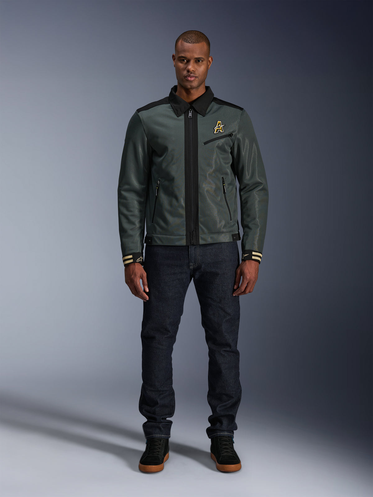 Casaco Alpinestars Ignite Air em Urban Gray Black Blue, casaco de motociclismo estilo Harrington com gola de camisa e construção em malha, usado por um homem com calças de ganga escuras e ténis pretos, vestuário urbano para motociclistas.