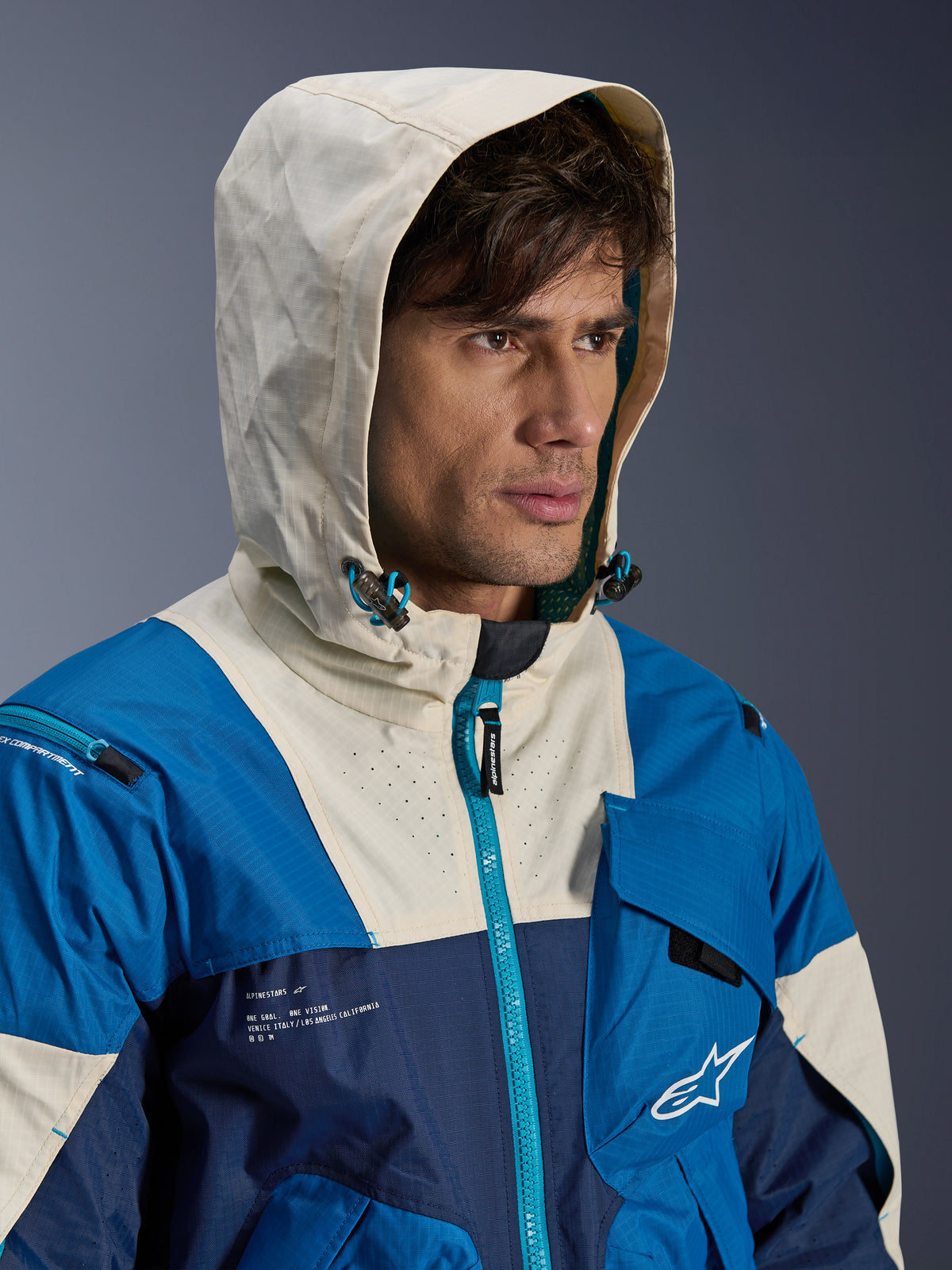Alpinestars Mogress Air, casaco de moto urbano para homem, azul e creme, em têxtil ventilado com capuz, modelo com o capuz colocado e detalhes técnicos.