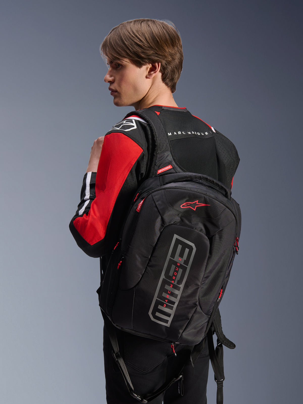Alpinestars MM93 City Hunter V2 Backpack, Black, featuring red Astars logo and grey MM93 branding, worn by a rider in a red and black motorcycle jacket, urban riding gear from the Marc Márquez collection