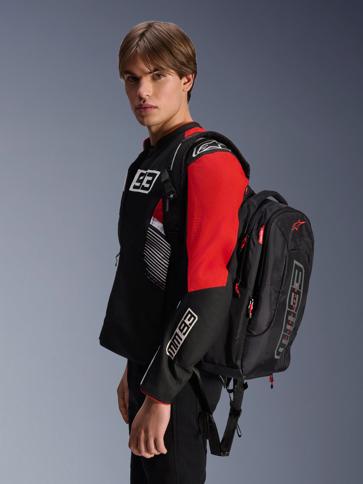 Alpinestars MM93 City Hunter V2 Backpack, Black with red accents, worn by a model in a matching black and red MM93 motorcycle jacket, featuring Marc Márquez branding and logos, urban riding apparel