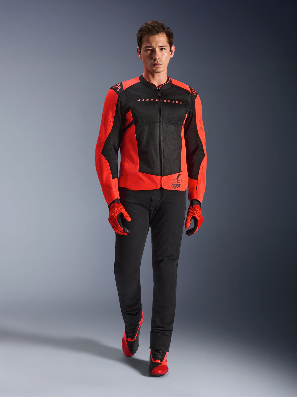 Casaco Alpinestars MM93 T-SPS Air V2, Vermelho Fluo e Preto, usado por um modelo com luvas vermelhas a condizer e calças pretas, com a marca Marc Marquez e o logótipo 93, casaco de motociclismo desportivo ventilado para condução urbana