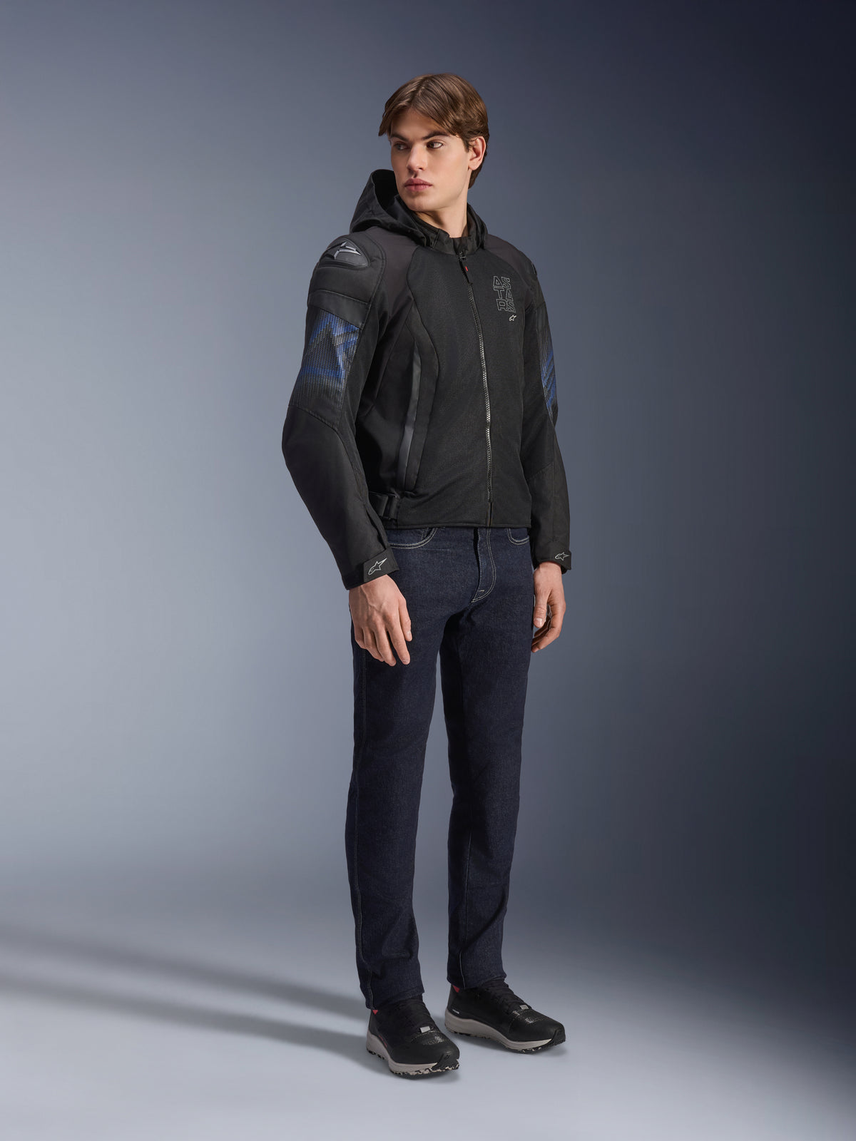 Alpinestars Zaca Air Venom WP Jacket, Black and Electric Blue textile motorcycle jacket, worn by model with dark jeans and black sneakers, featuring a detachable hood, mesh ventilation panels, and DFS Lite shoulder sliders, sporty all-weather riding gear.