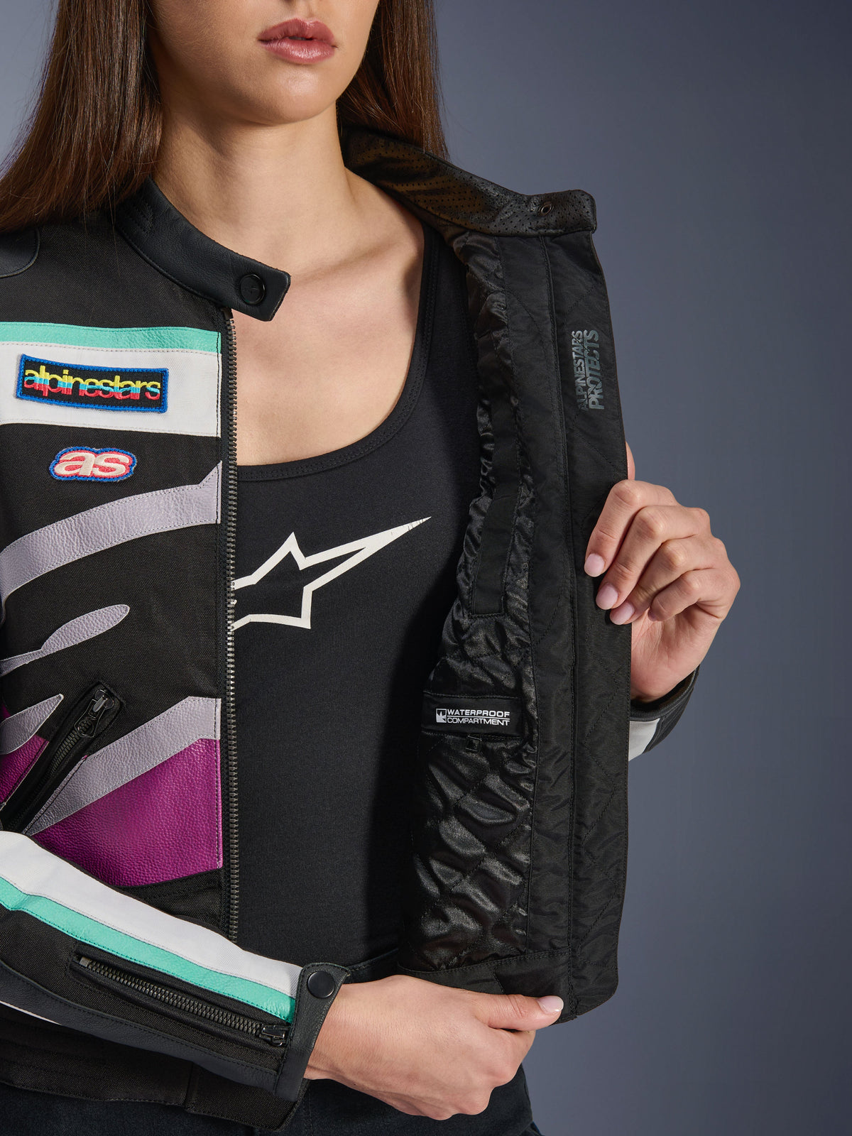 Casaco Feminino Alpinestars Idles, preto, off white e roxo, vista aproximada do forro interno acolchoado com compartimento impermeável, com emblemas de corrida de inspiração vintage e pormenores coloridos em verde-água e roxo no exterior em tecido