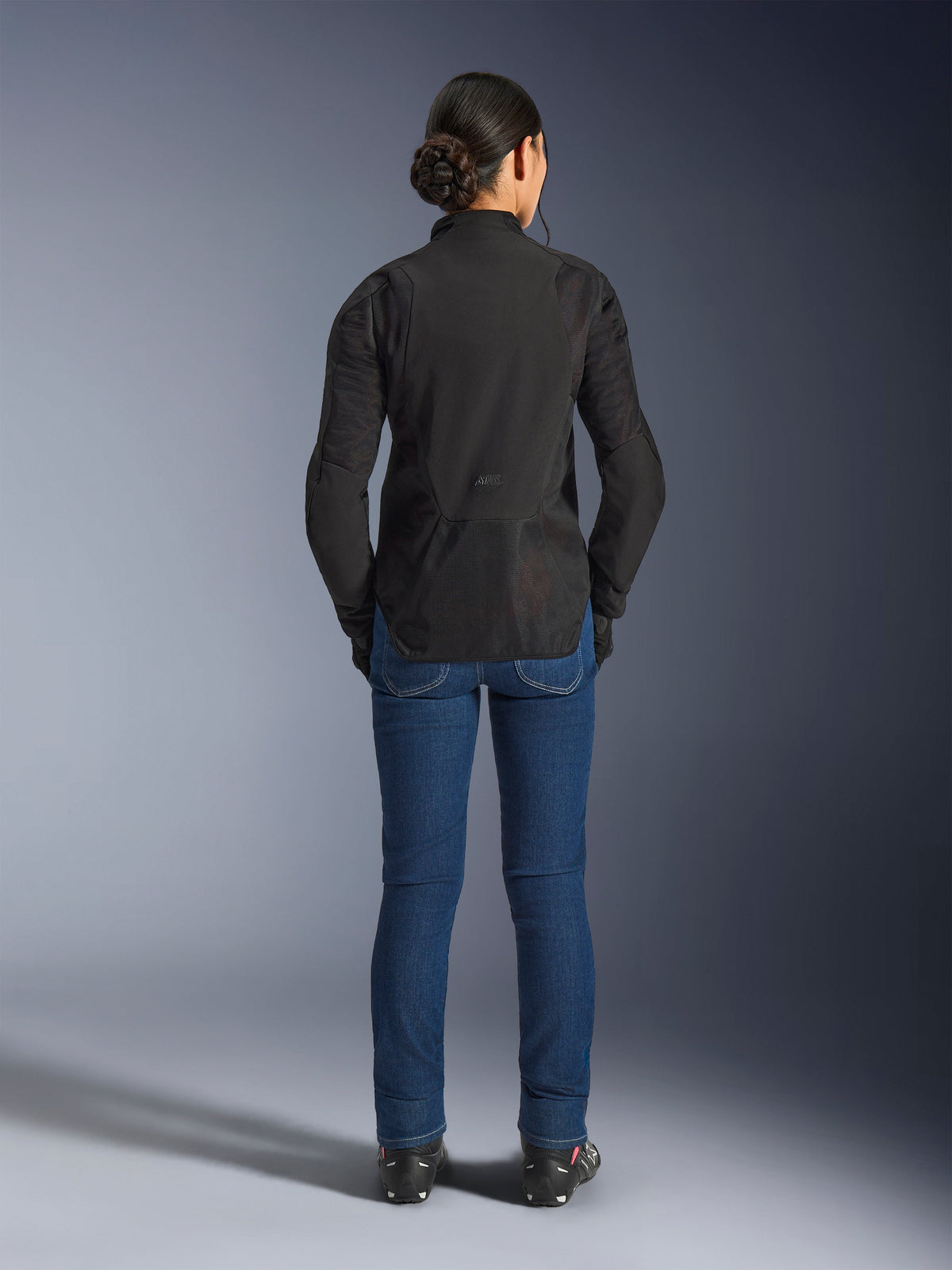 Woman Stella Aeroshell Airflow Jacket, Black Anthracite, back view on a model, featuring lightweight softshell chassis with laser-perforated mesh panels, extended rear profile for coverage, sport riding fit, paired with blue jeans