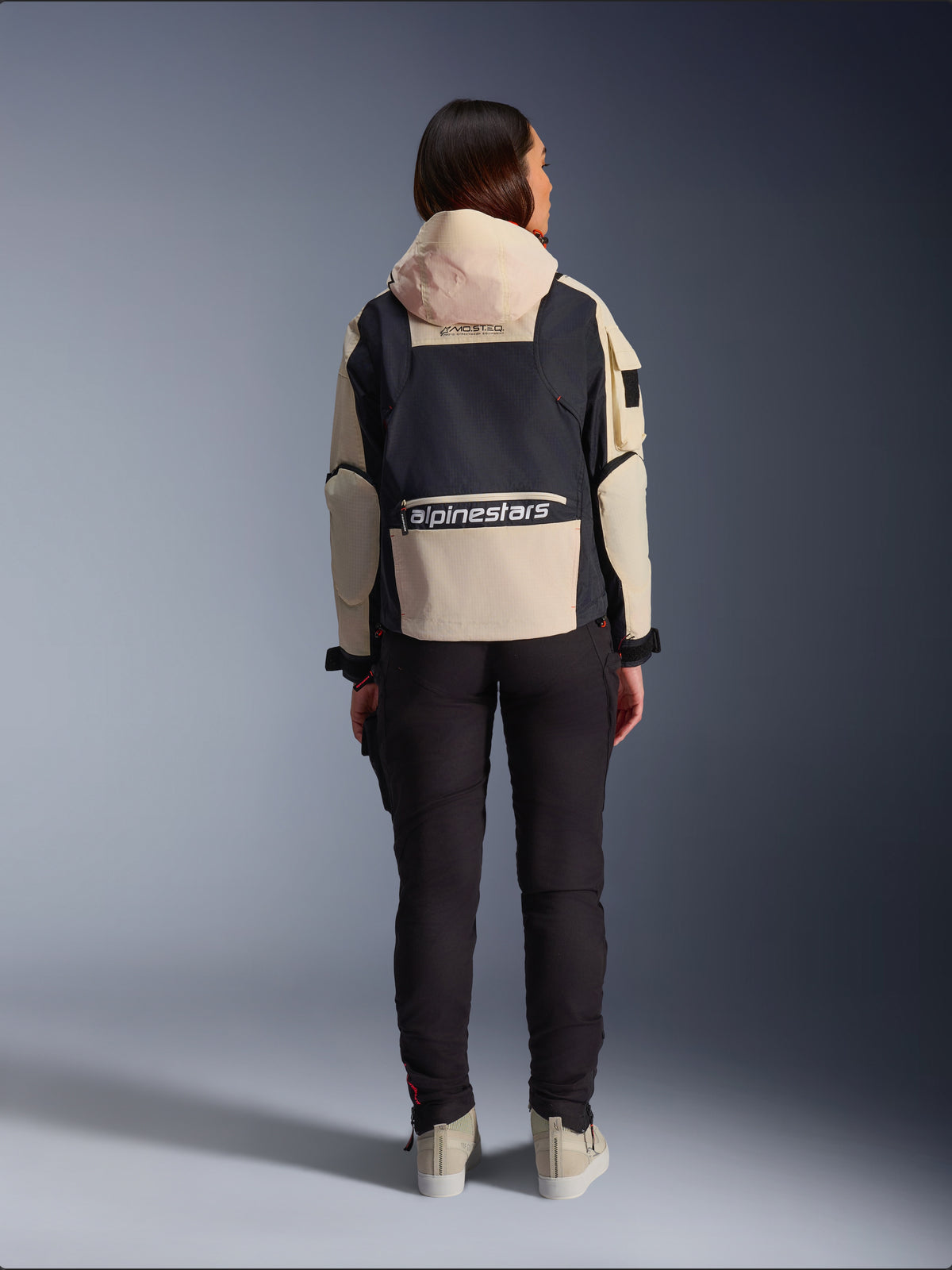 Alpinestars Molly Air Jacket, casaco de motociclismo para mulher, Black Almond, vista traseira mostrando o capuz e o logótipo grande nas costas, design ripstop de inspiração utilitária, combinado com calças de condução pretas.