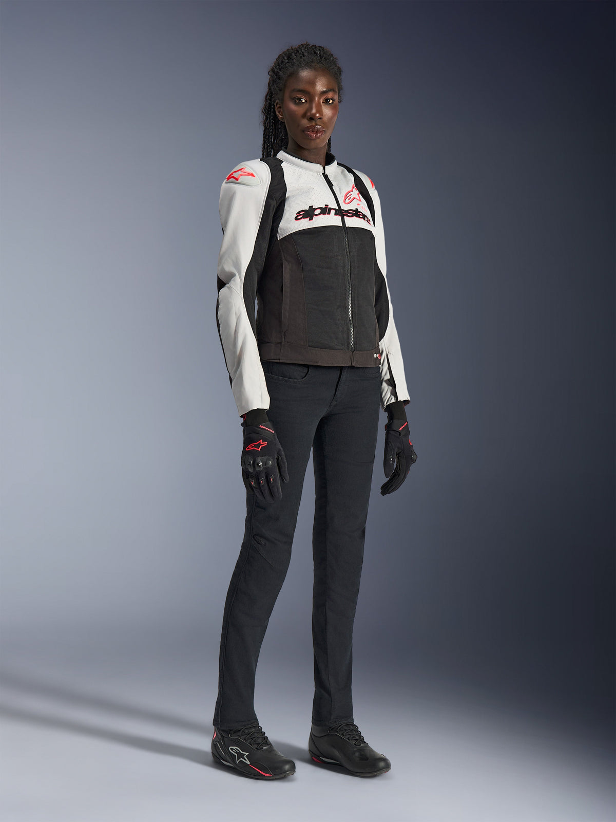 Alpinestars Casaco Stella SMX Air em Cinzento Gelo, Preto e Coral Fluo, vestido por uma modelo com calças e luvas de motociclismo pretas, apresentando construção em malha e logótipos vermelho coral, equipamento desportivo de motociclismo para mulher