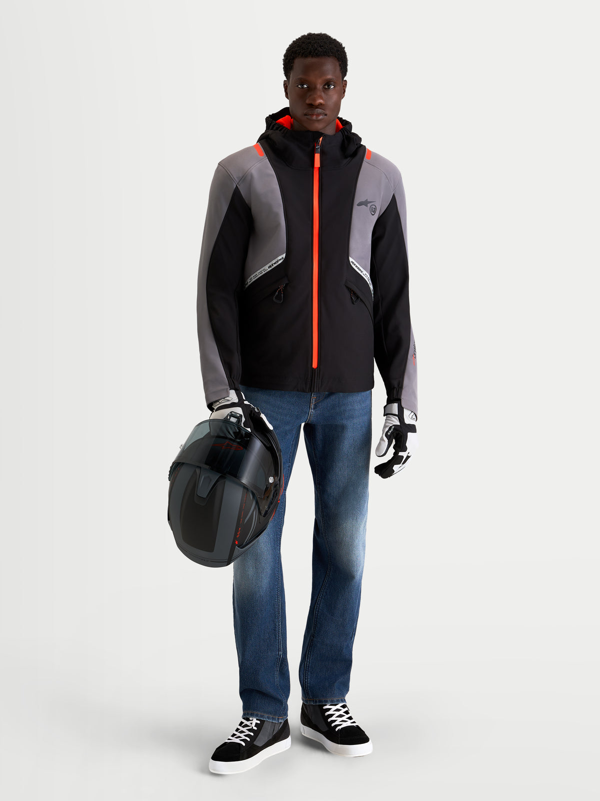 Alpinestars Flex-AST 8 Denim calças de ganga de moto para homem em azul médio, vestidas por um modelo que segura um capacete e veste um casaco técnico preto e cinzento