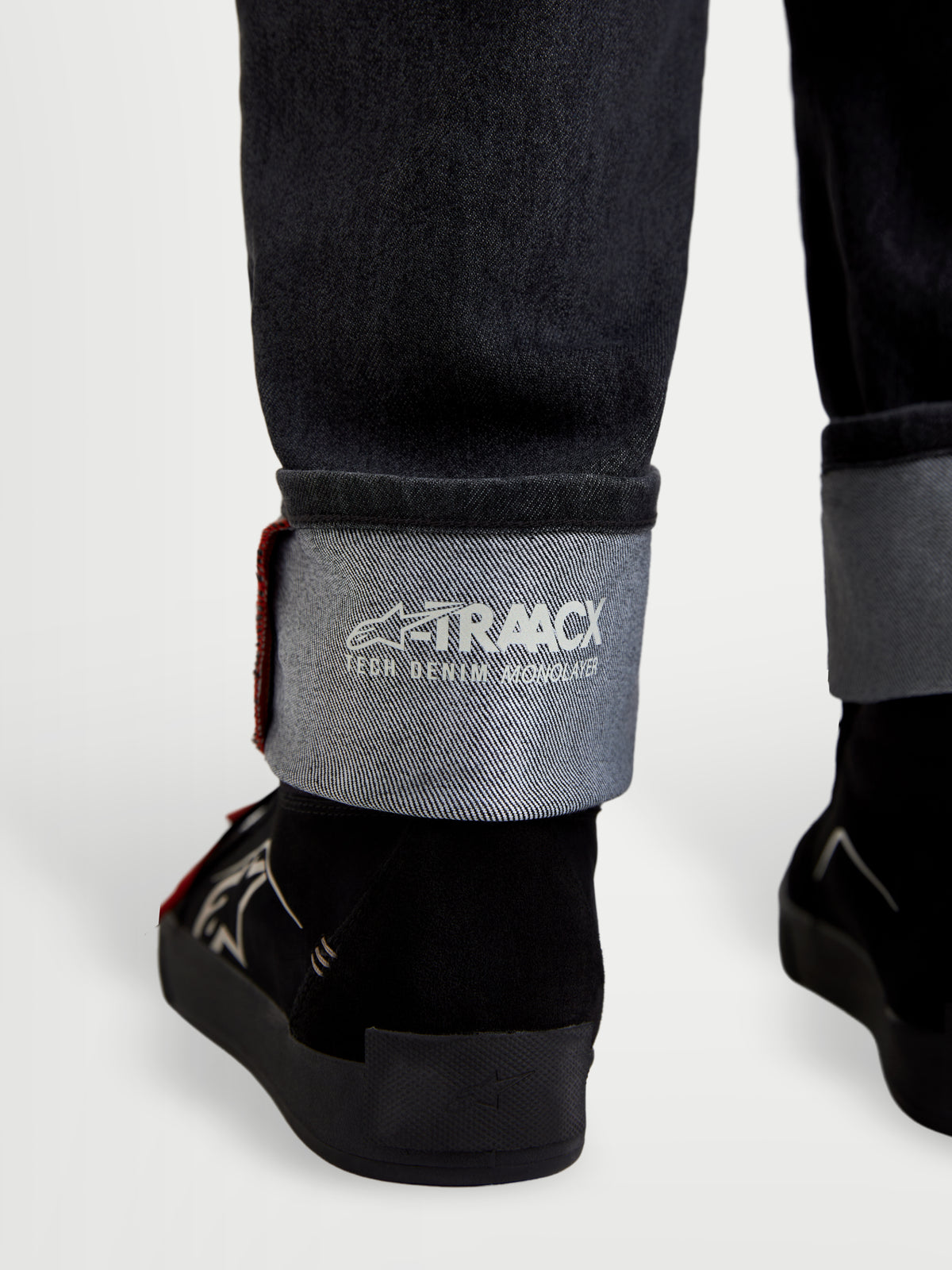 Alpinestars Flex-AST 7 Denim Pants, motorcycle denim pants in faded black, close-up view of cuffed hem showing A-TRAACX technical denim branding and selvedge detail