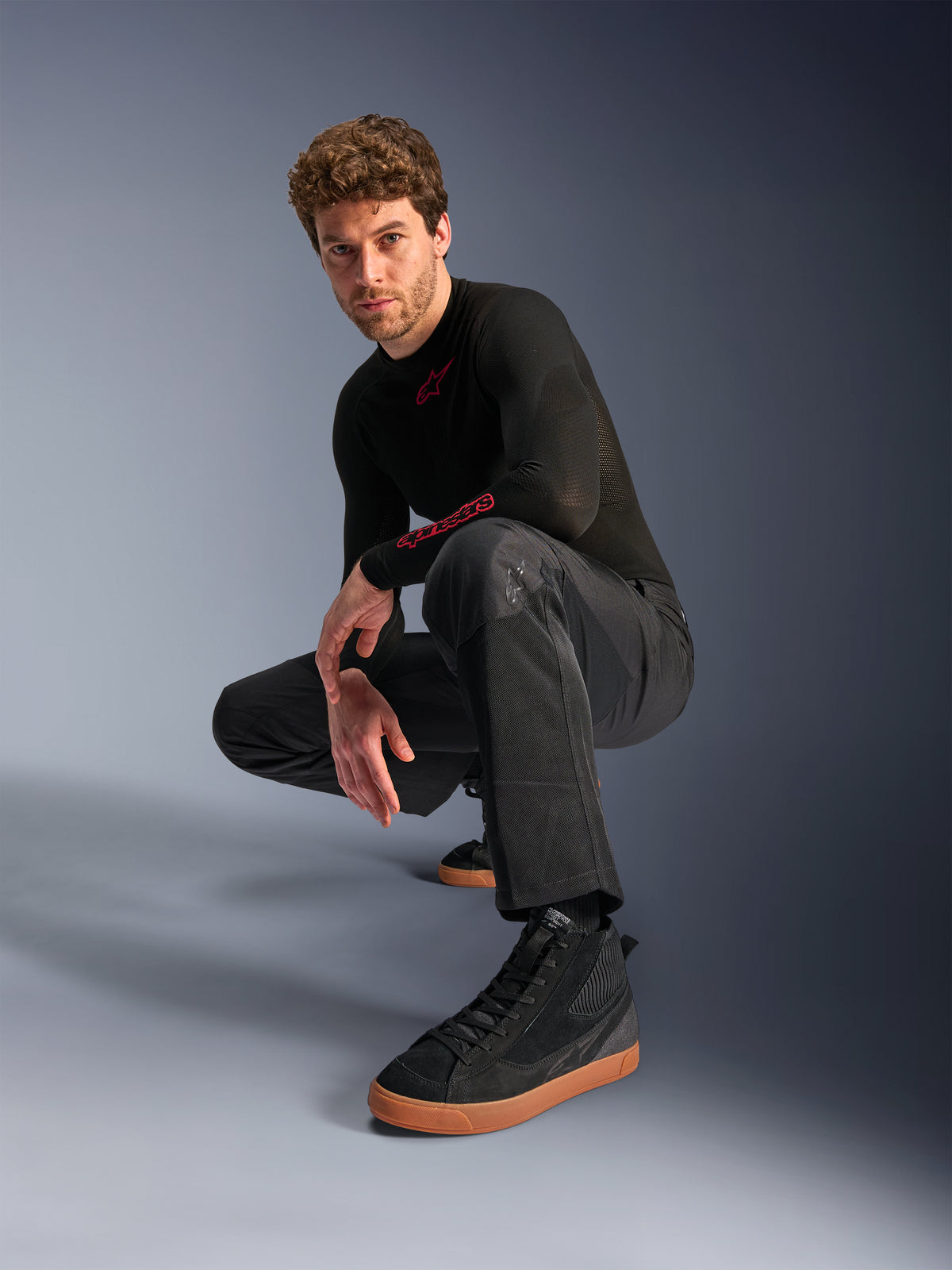 Alpinestars C-1 Air Pants, Urban Motorcycle Pants, Black, model crouching in a studio setting, worn with a black long-sleeve top and black sneakers with tan soles, featuring breathable mesh panels and a contemporary urban style