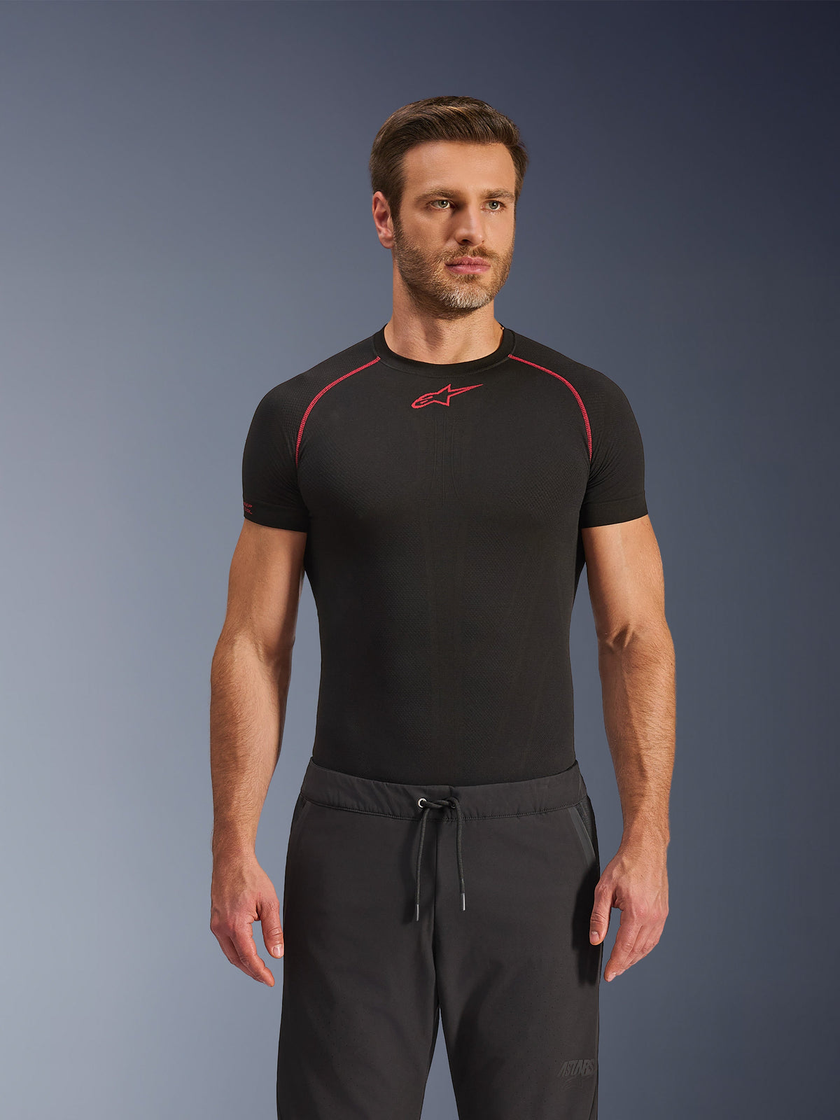 Calças Alpinestars Aeroshell Airflow, calças de motociclismo pretas, em tecido softshell leve, com cintura ajustável por cordão e ventilação perfurada a laser, usadas com uma camisola de base preta da Alpinestars