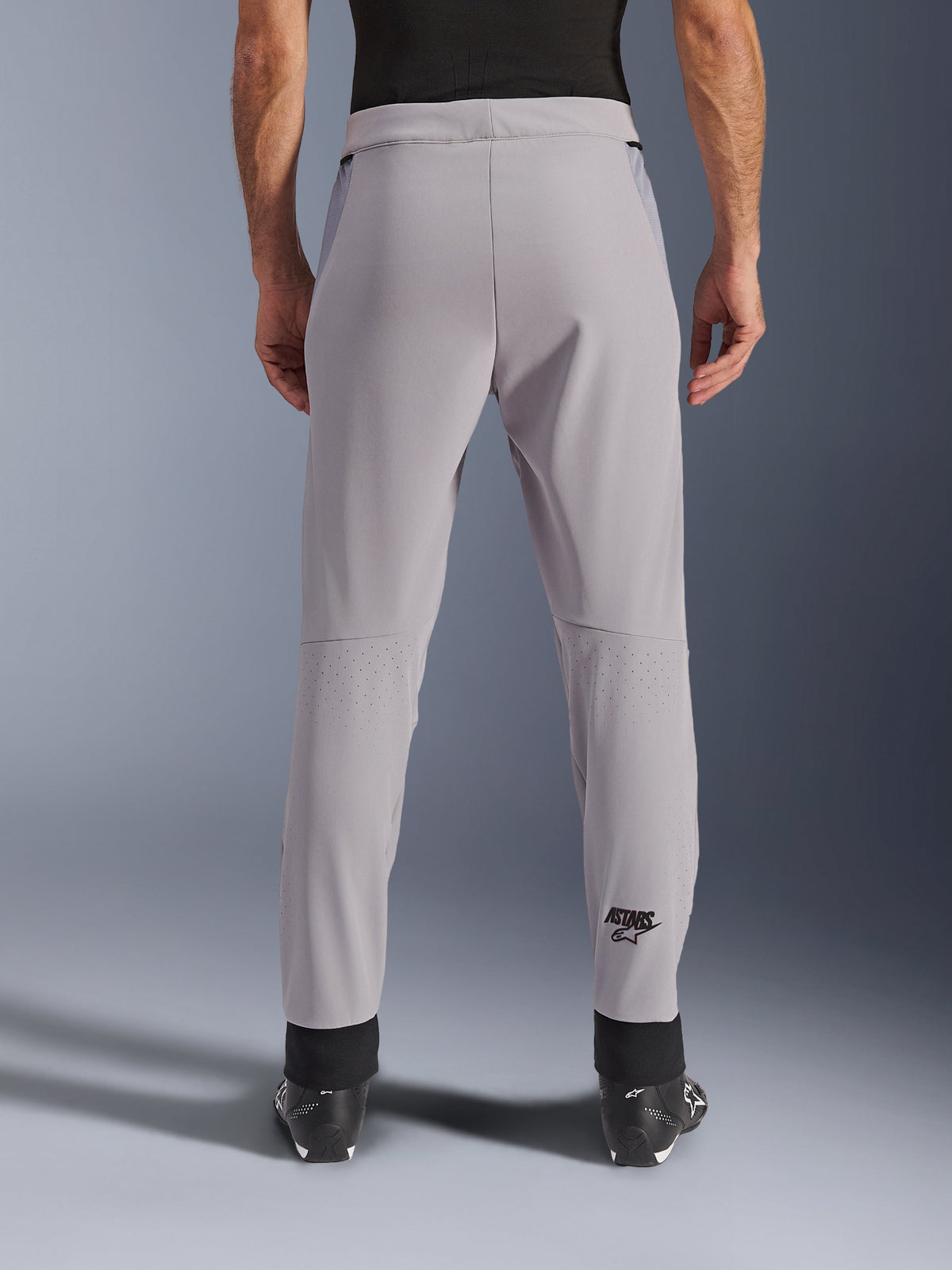 Calças Alpinestars Aeroshell Airflow, calças de motociclismo, cinzento médio, vista traseira mostrando zonas perfuradas a laser nas panturrilhas e logótipo Astars preto, construção em têxtil softshell com punhos pretos nos tornozelos e painéis de malha nas ancas.