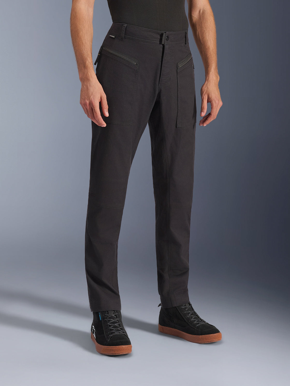 Alpinestars Flex-AST Canvas Pants, calças de motociclismo urbanas, pretas, usadas por um modelo com sapatilhas pretas, com um design clássico de roupa de trabalho, tecido de sarja de policotão elástico e bolsos frontais funcionais com fecho de correr