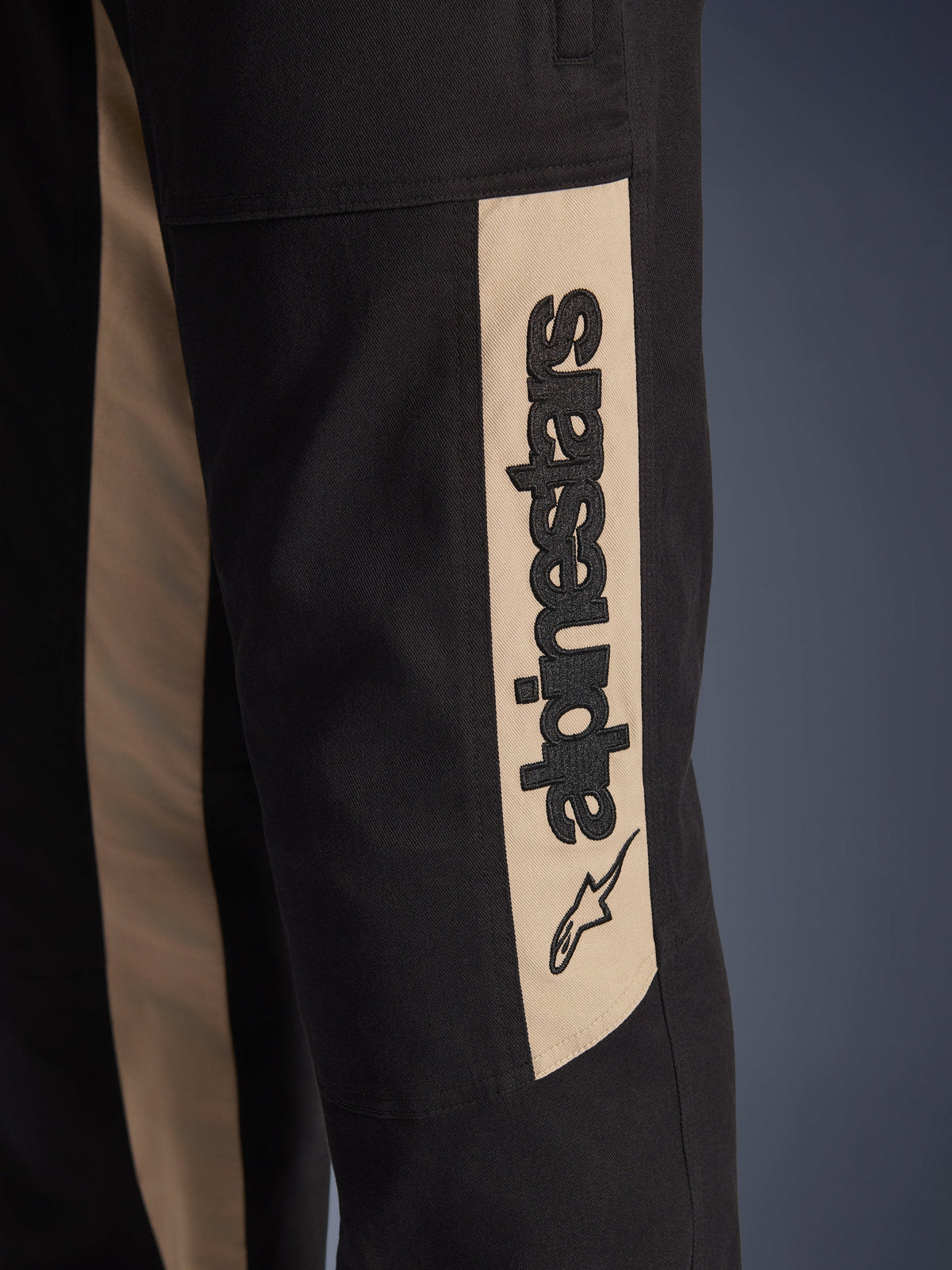 Calças Alpinestars Flex-AST Canvas, detalhe em grande plano da lateral da perna, pretas com painel de realce em tom alumínio, com logótipo Alpinestars vertical e ícone de estrela em preto, sarja de policotão durável para condução urbana de motociclo