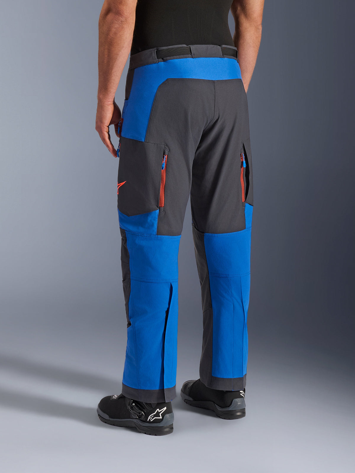Calças Alpinestars Maxdura Dual, em Azul Royal e Cinzento Escuro, vista traseira com bolsos com fecho e zonas de ventilação, design sobre a bota com botas Alpinestars pretas, equipamento durável para aventura e dual-sport