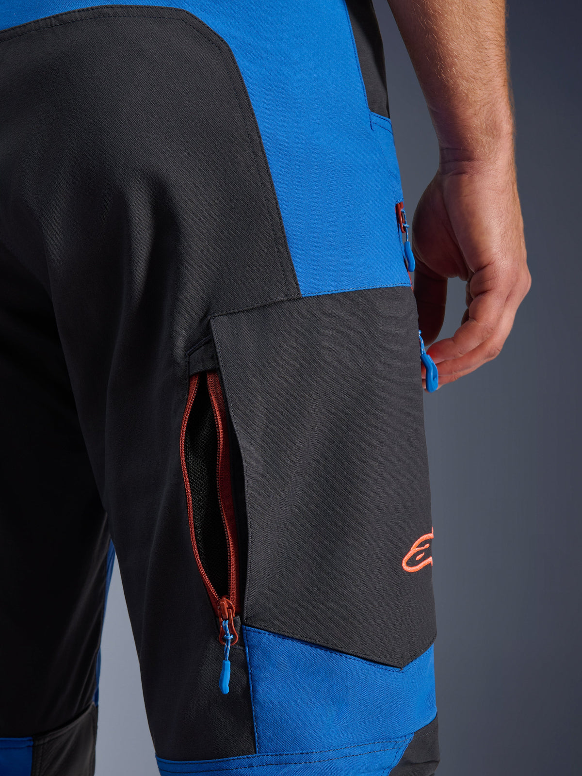Alpinestars Maxdura Dual Pants, azul royal e cinzento escuro, pormenor do bolso cargo lateral com fecho, puxadores de fecho azuis, logótipo bordado a laranja, equipamento de motociclismo de aventura