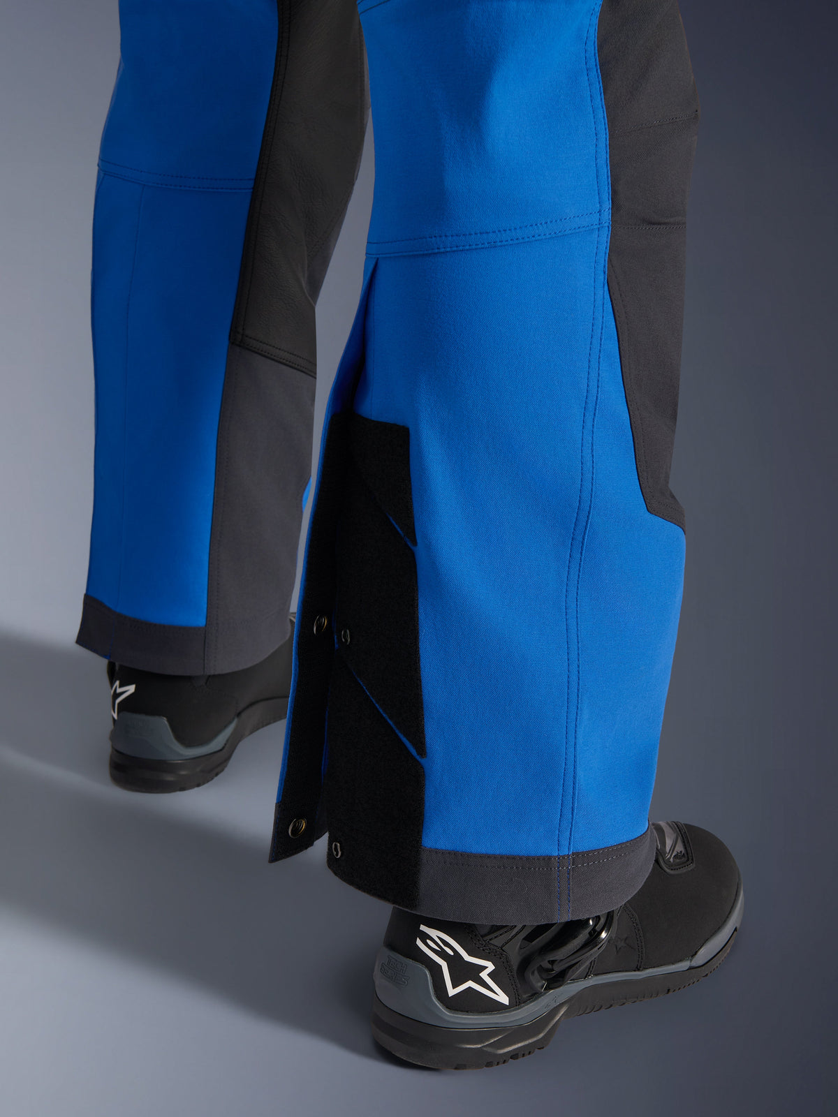 Calças Alpinestars Maxdura Dual, Azul Royal e Cinzento Escuro, grande plano da parte inferior da perna ajustável com fechos de pressão e fole, design de corte adventure sobre a bota, usadas com botas de motociclismo Alpinestars pretas