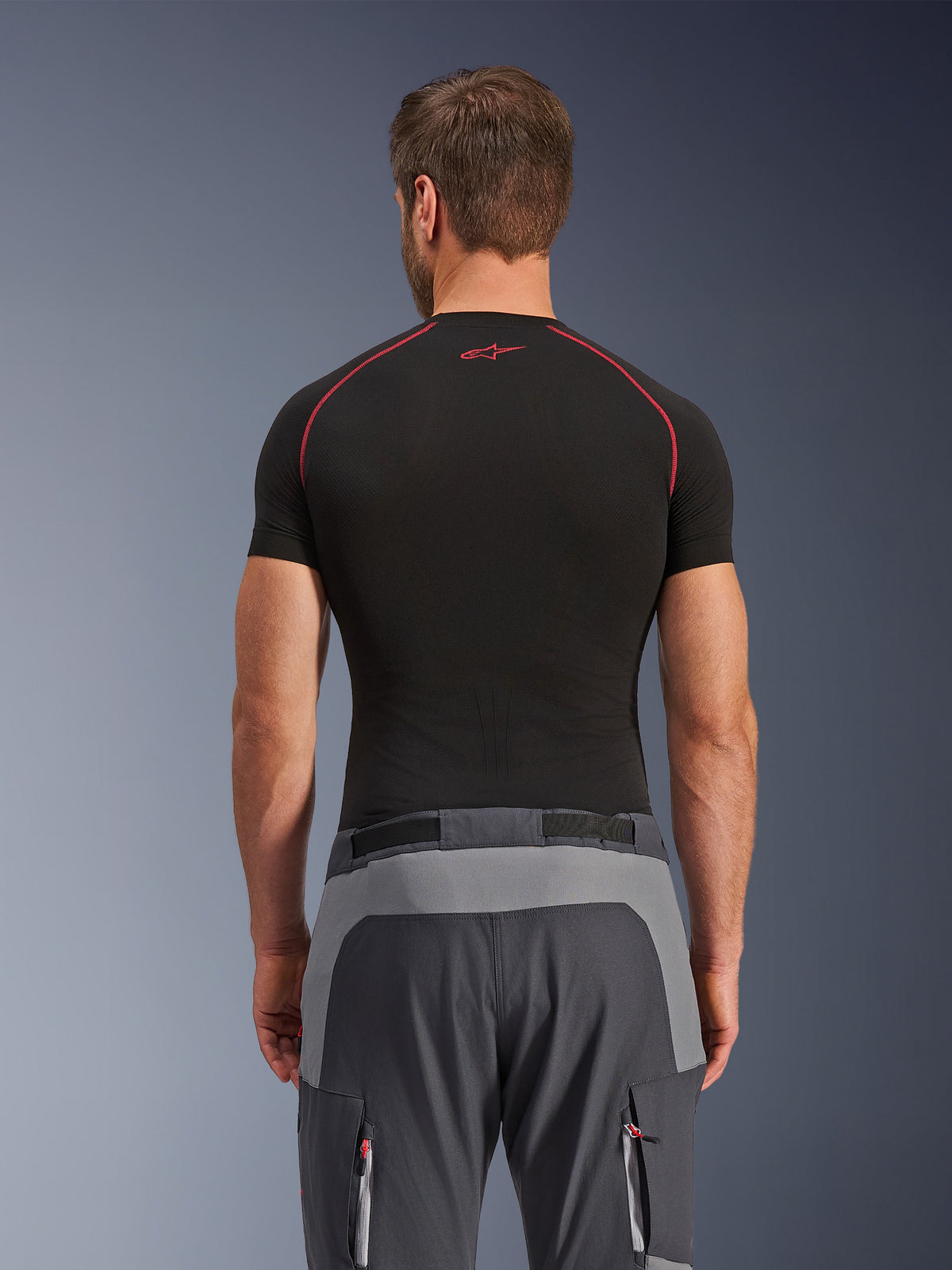 Alpinestars Maxdura Dual Pants, calças de motociclismo de aventura, cinzento escuro e cinzento profundo, vista traseira com painéis reforçados no assento e na cintura, usadas com uma camada base de manga curta preta, com bolsos com fecho de correr e detalhes vermelhos