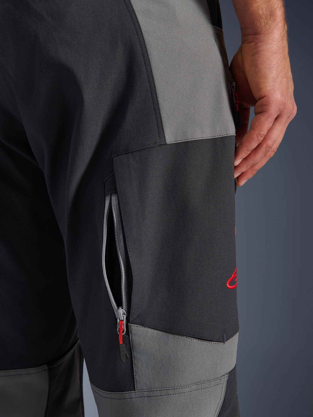 Alpinestars Maxdura Dual Pants, calças de motociclismo de aventura em Cinzento Escuro e Cinzento Profundo, grande plano da coxa com abertura de ventilação com fecho de correr e logótipo bordado a vermelho, construção em poliamida elástica durável.