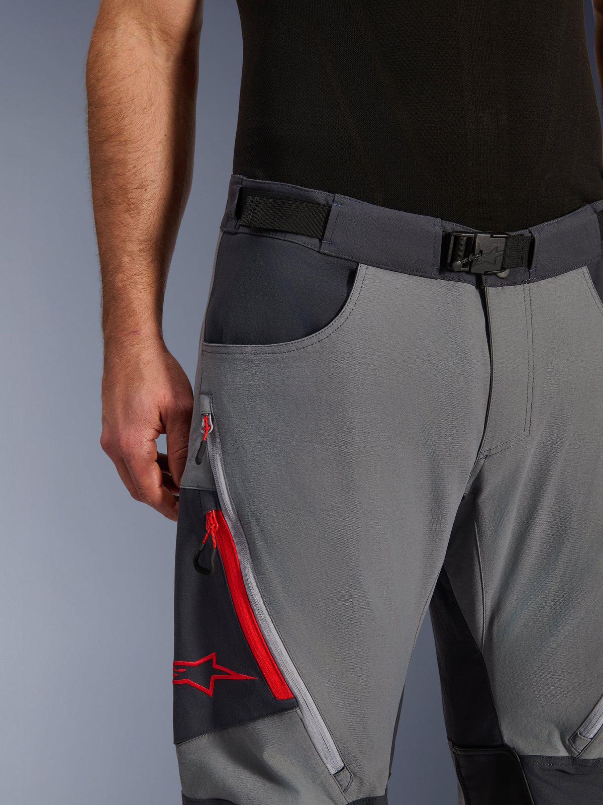 Alpinestars Maxdura Dual Pants, calças de motociclismo de aventura, cinzento escuro e cinzento profundo, pormenor do cinto ajustável na cintura com fivela magnética, bolso cargo com fecho de correr com detalhes em vermelho e logótipo Alpinestars.
