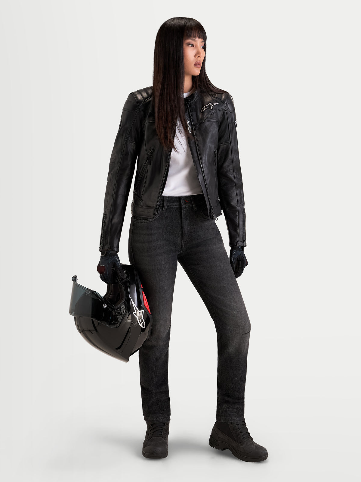 Alpinestars Stella Flex-AST 7 Denim calças de moto para mulher, ganga preta desbotada, com conforto COOLMAX, num modelo a segurar um capacete e um casaco de pele a condizer