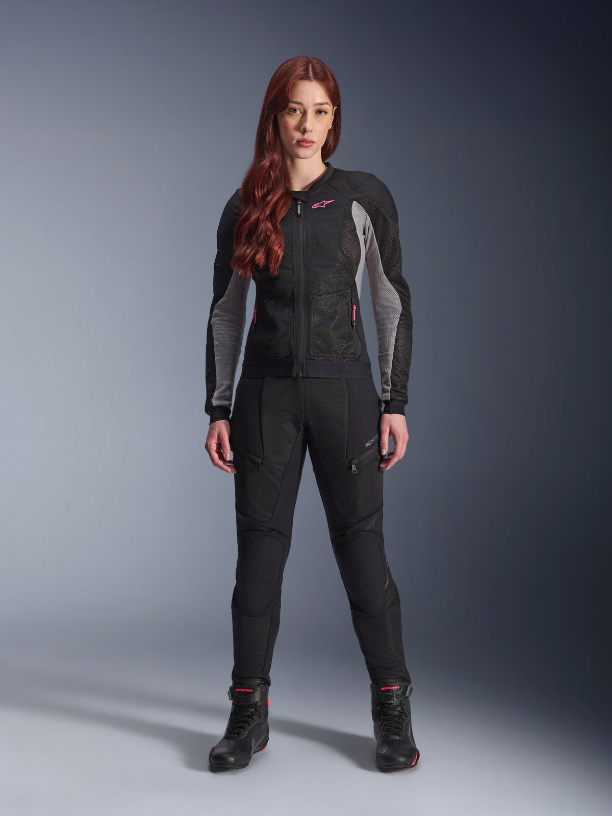Alpinestars Stella Troop-Air Pants, calças de motociclismo para mulher em preto, com painéis de malha e bolsos com fecho, combinadas com um casaco de malha preto e cinzento com detalhes rosa e botas de condução pretas, equipamento de motociclismo urbano completo