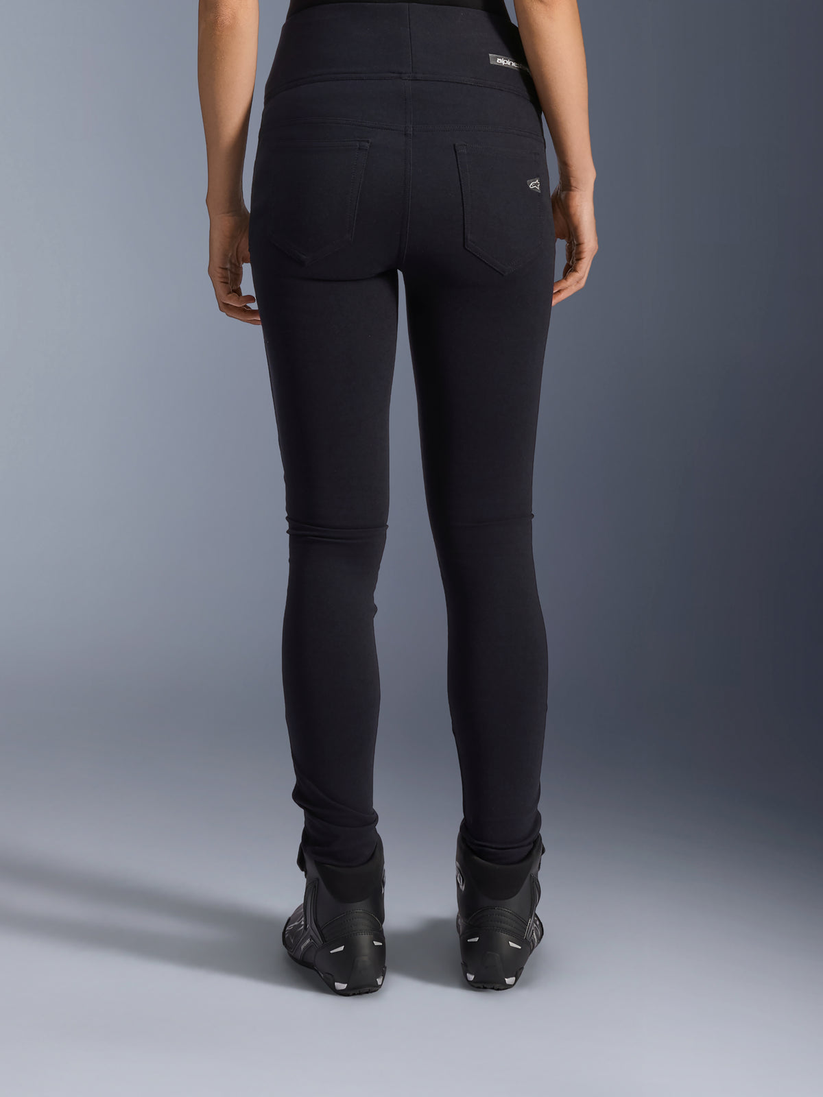 Alpinestars Stella Flex-Ast Leggings, leggings de motociclismo para mulher, pretas, vista traseira mostrando os bolsos e o ajuste justo, usadas com botas de motociclismo pretas, estilo de condução urbano