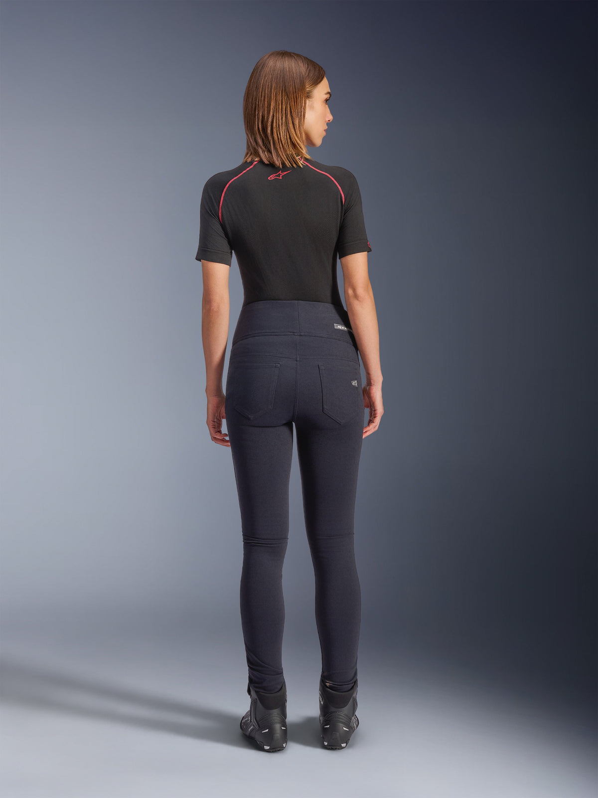Alpinestars Stella Flex-AST Leggings em preto, calças de motociclismo de cintura subida para mulher, vista traseira mostrando o corte justo e os bolsos traseiros, usadas com top de manga curta preto e botas de condução, equipamento de condução urbano