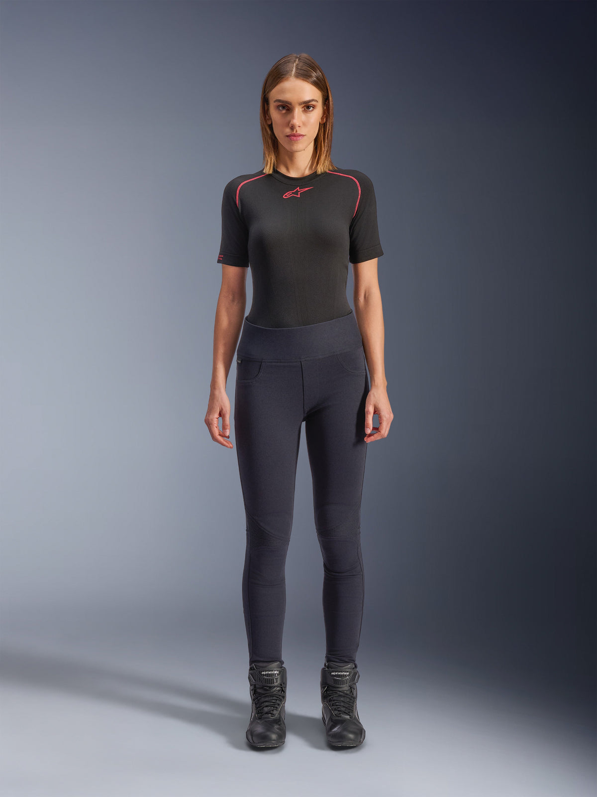 Alpinestars Stella Flex-Ast Leggings, leggings de motociclismo para mulher, pretas, usadas com um top preto de manga curta com detalhes vermelhos e botas de motociclismo pretas, equipamento de condução urbana contemporâneo de corte justo, vista frontal